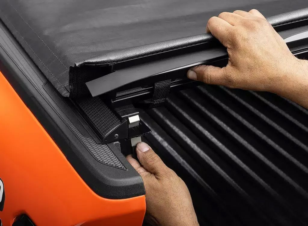 Hands opening a black tonneau cover on an orange truck bed