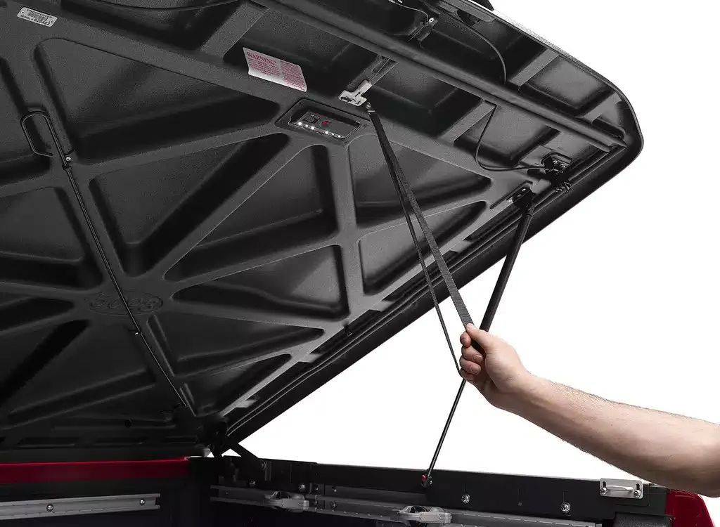 Hand lifting a car hood with a support strut, showing the black underside and engine bay.