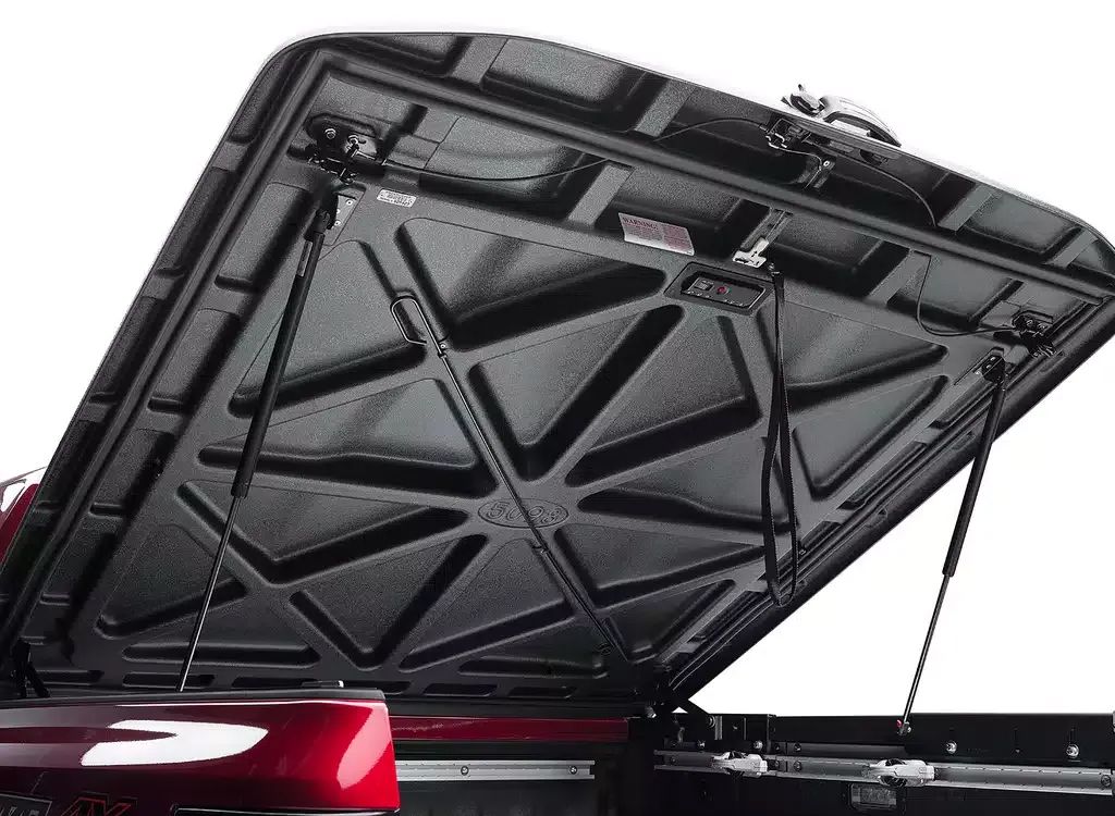 Open truck bed cover lifted open, showing the underside support structure and red tail light area