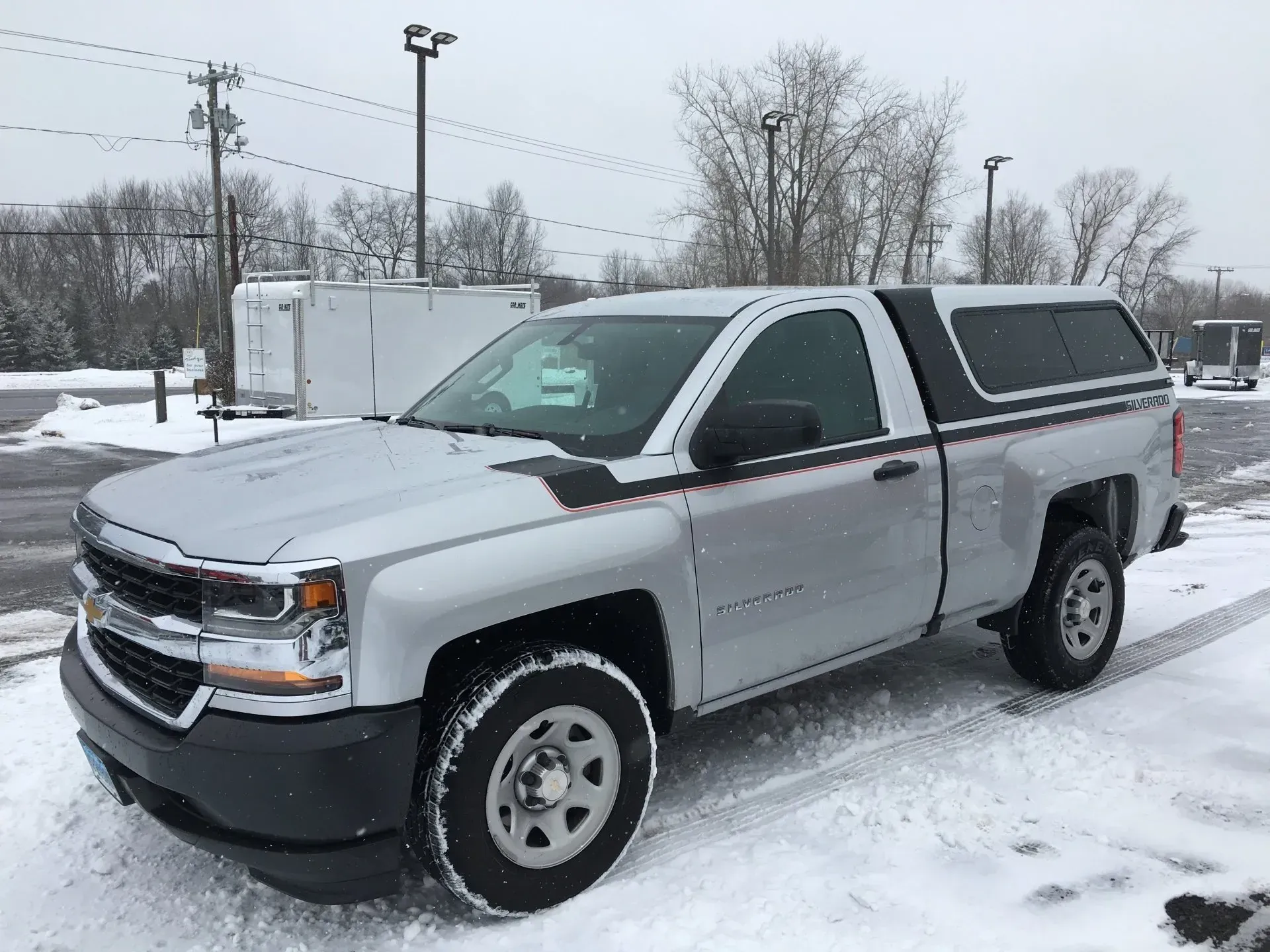Silver Chevrolet pickup truck parked in a snowy lot under an overcast sky