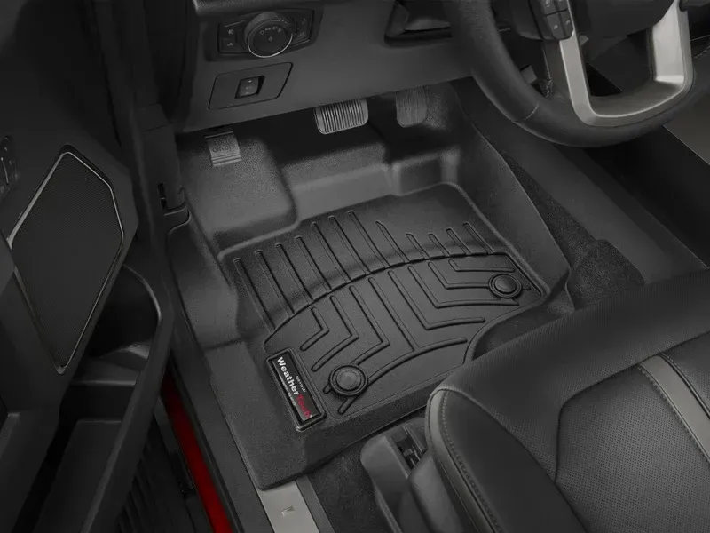 Car floor mat with raised grooves in a black car interior near the pedals and seat