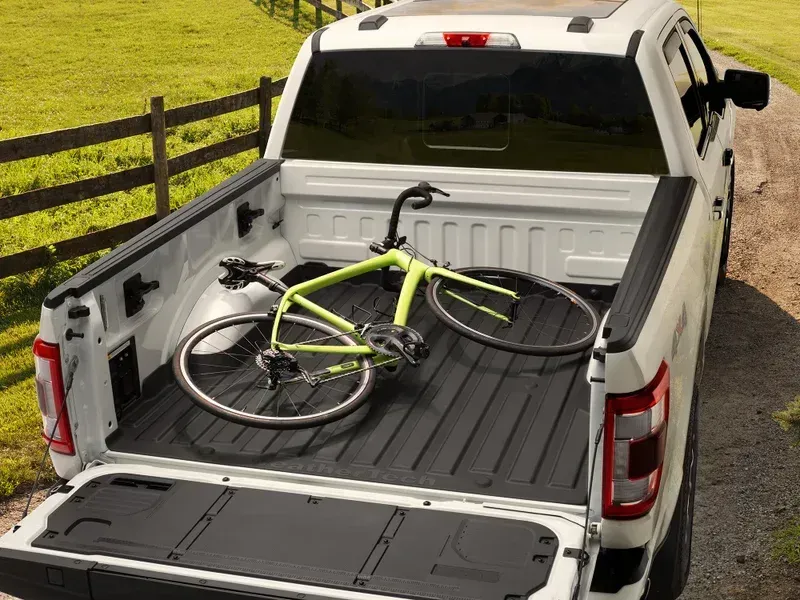 White pickup truck bed with a lime green bicycle lying inside on a rural road near a fence
