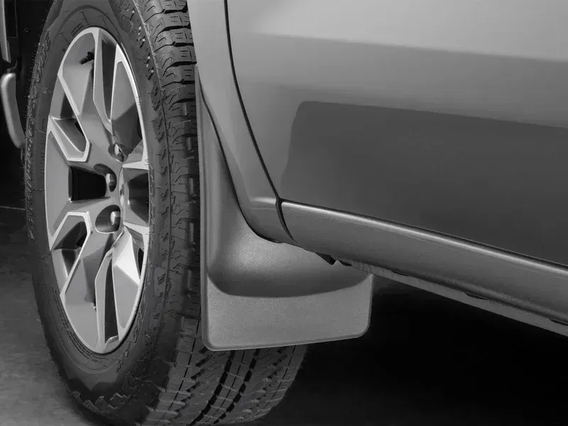 Close-up of a gray SUV wheel and rear mud flap on a paved road