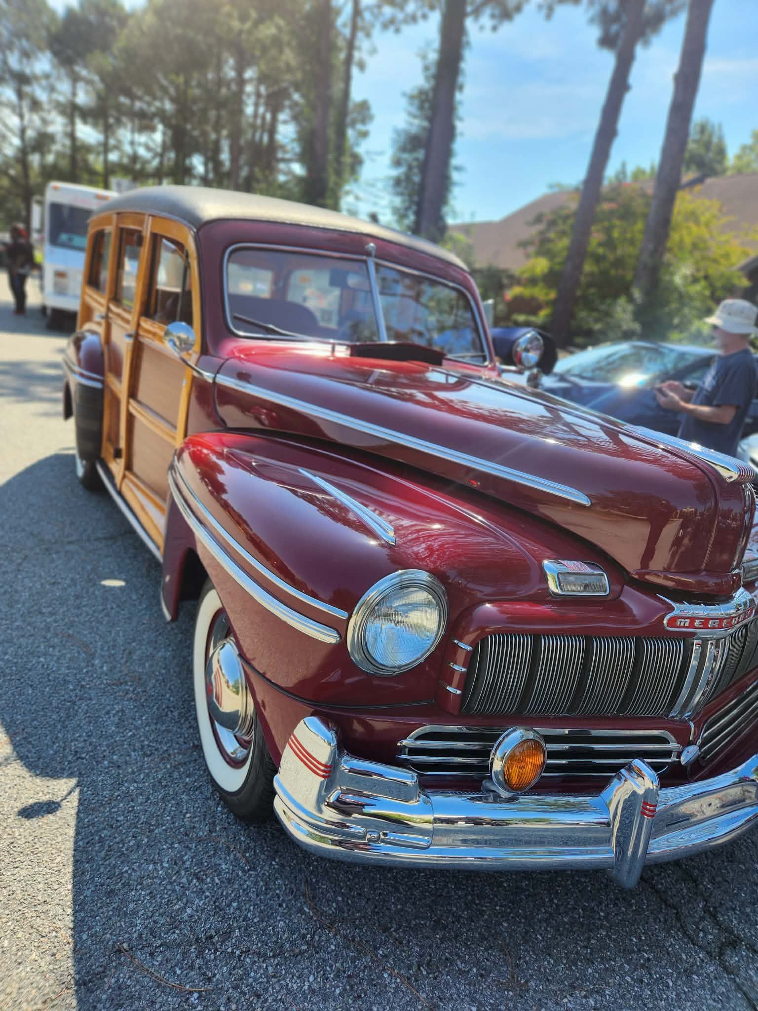 Maroon vintage woodie station wagon parked outdoors on a sunny street with trees in the background.