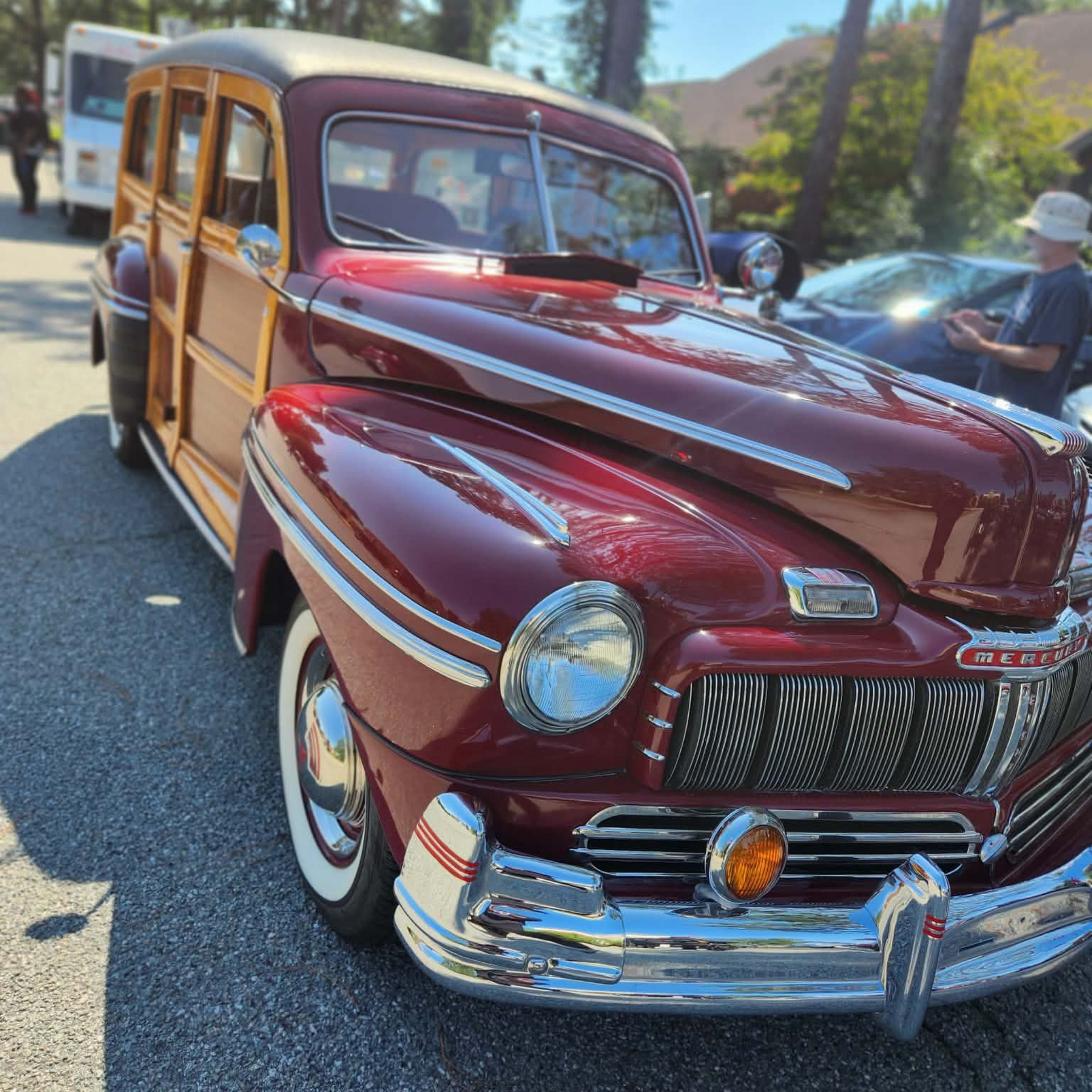 Maroon vintage woodie station wagon parked outdoors on a sunny street with trees in the background.