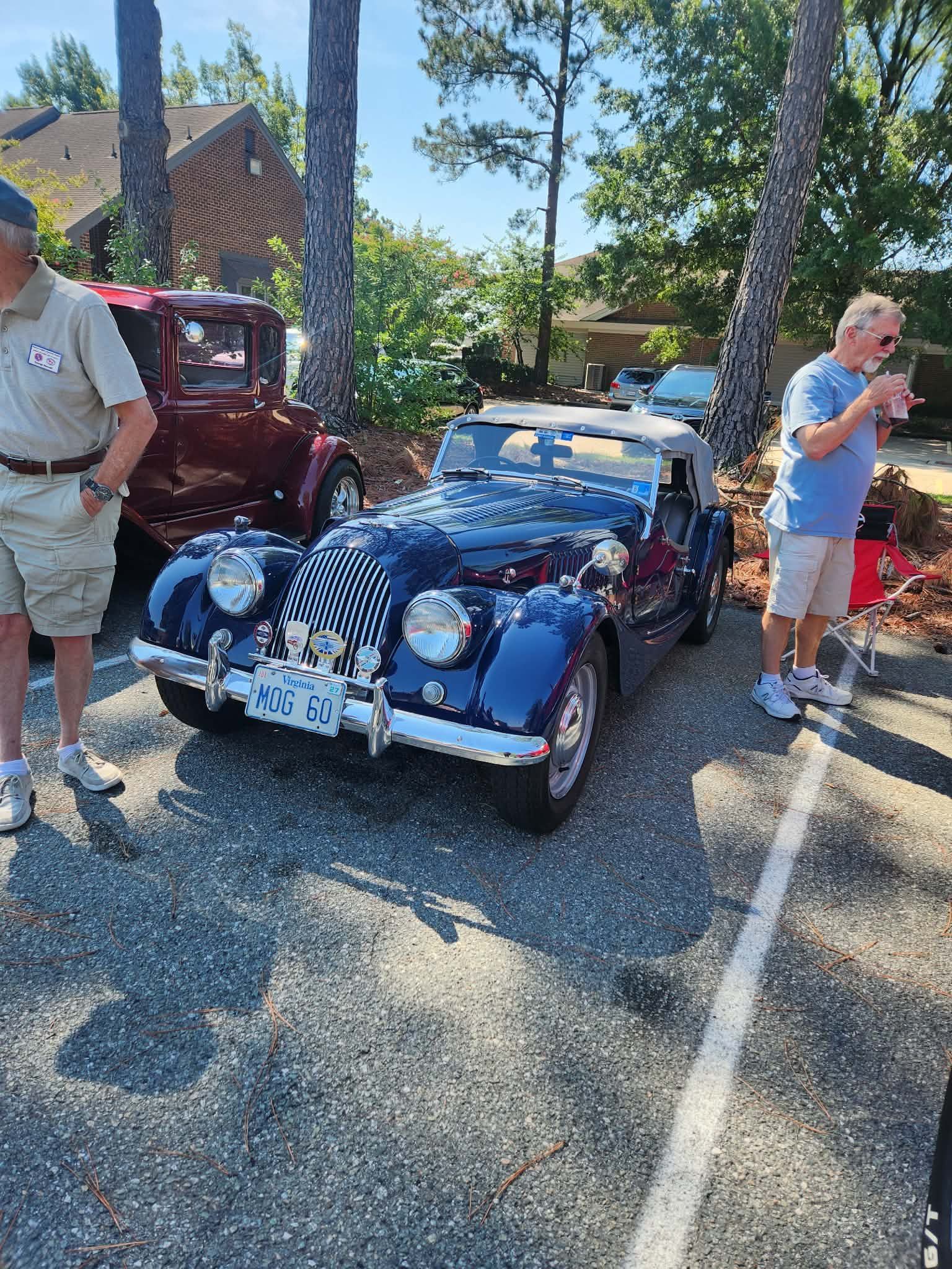 Blue vintage convertible with white stripes parked outdoors, surrounded by people in a sunny lot.