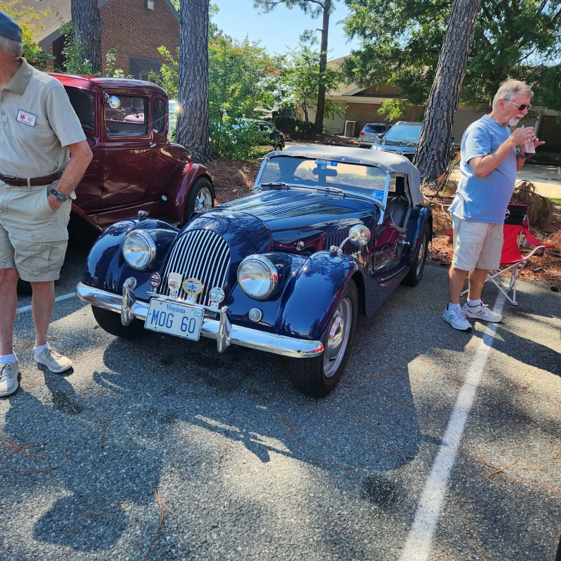 Blue vintage convertible with white stripes parked outdoors, surrounded by people in a sunny lot.