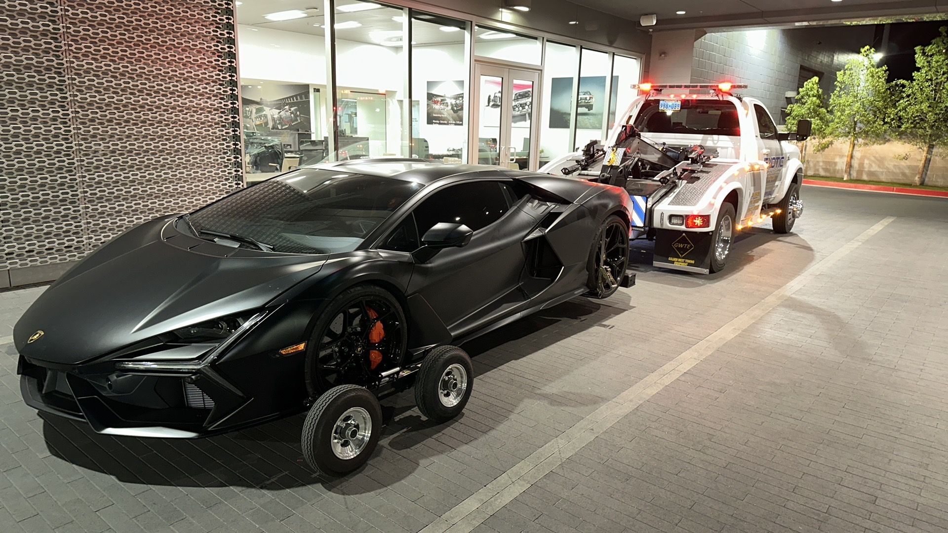 An exotic car being towed by a truck towing in front of a building