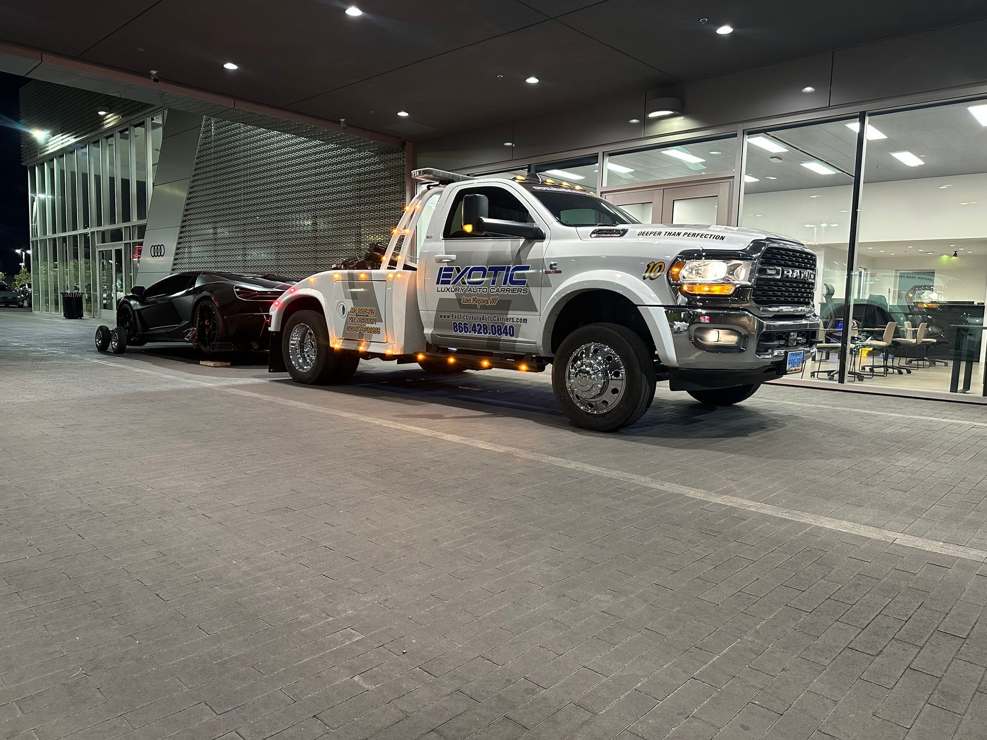 A truck towing an exotic car in front of a building