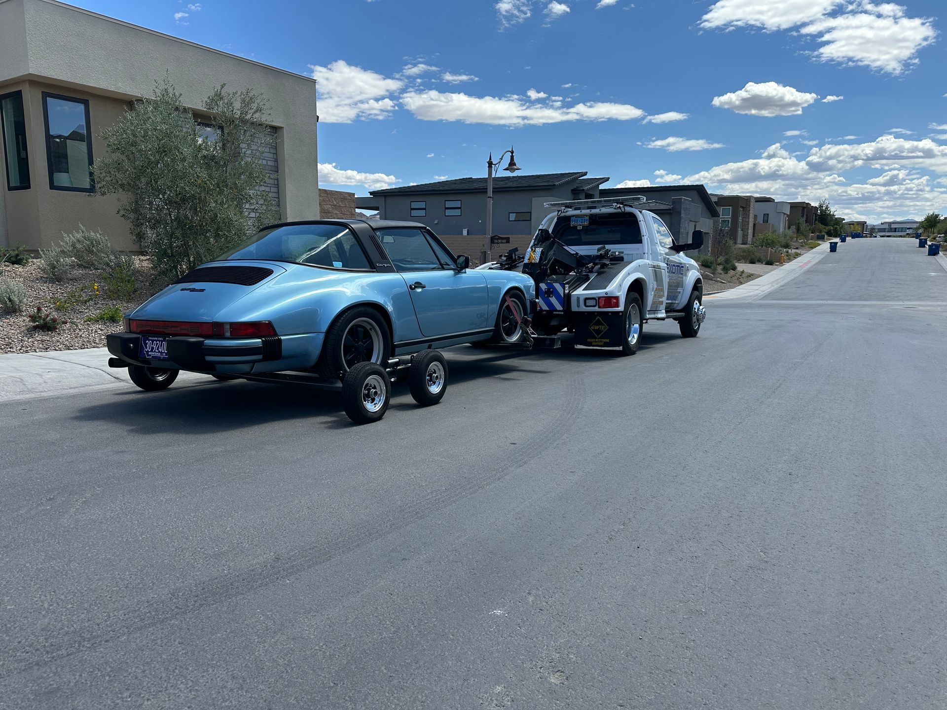blue sports car on trailer behind white tow truck