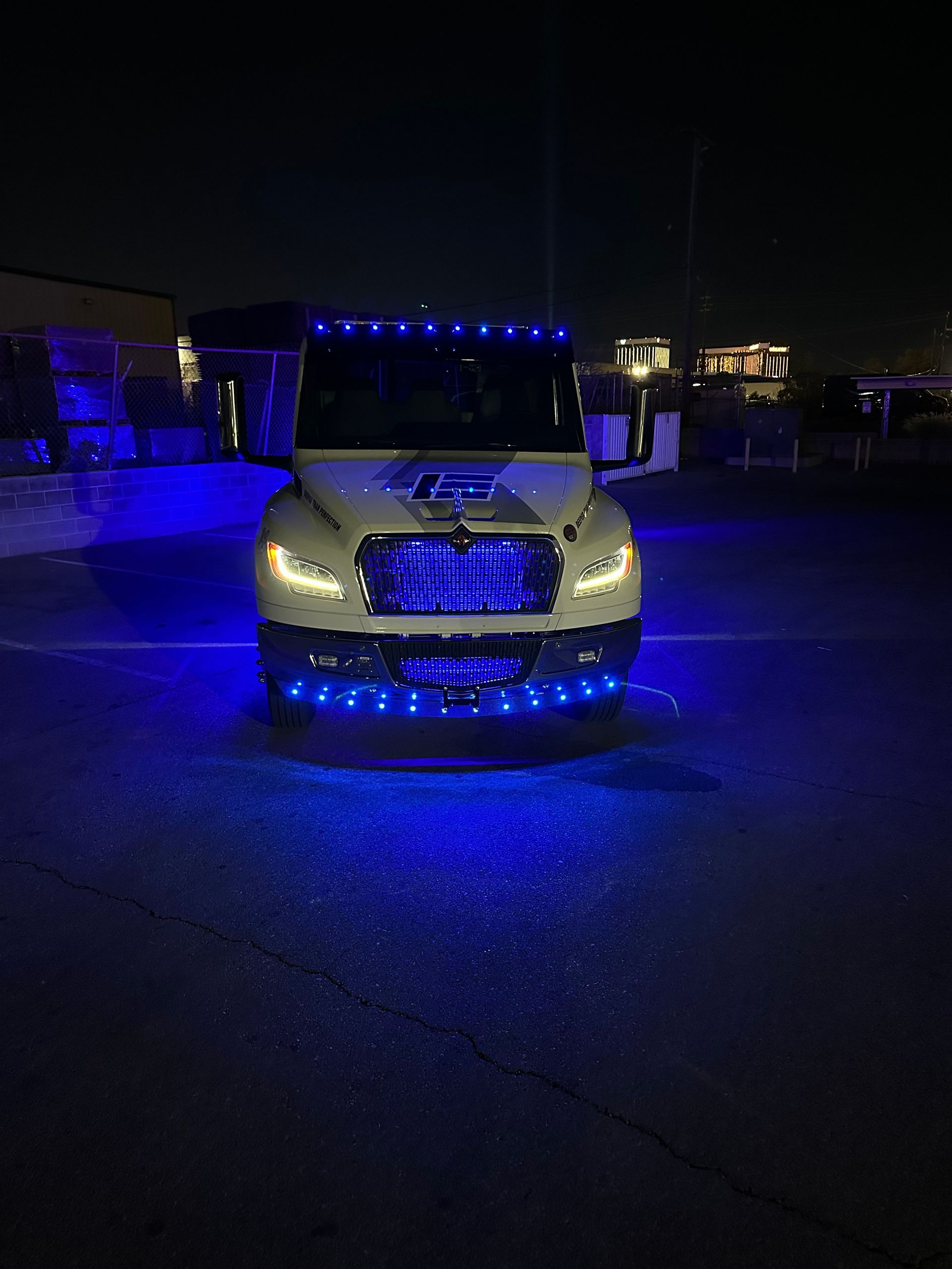 White truck with blue LED lights on grill and above the windshield, at night.