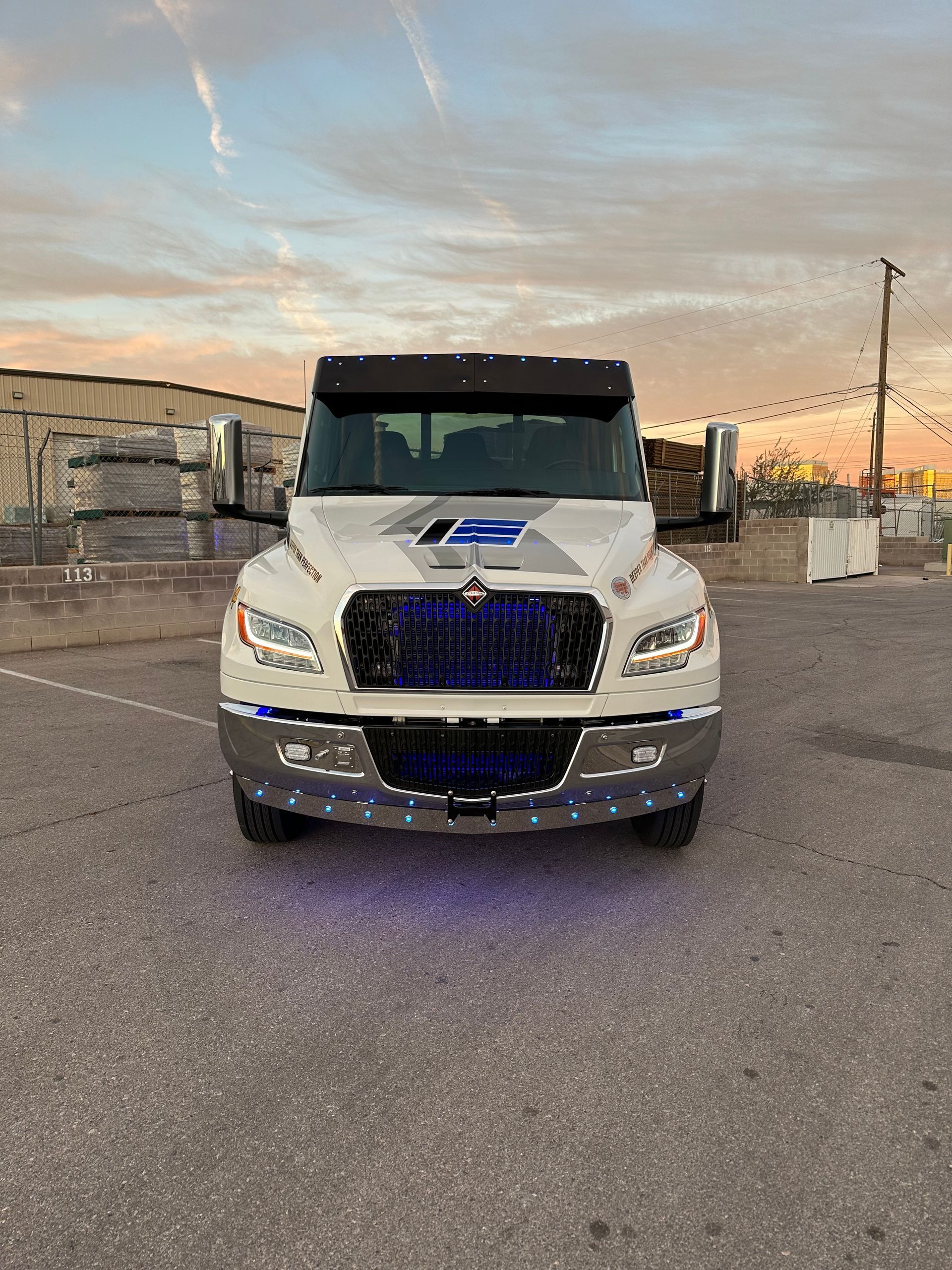 White truck with blue lights on a concrete surface, sunset background.