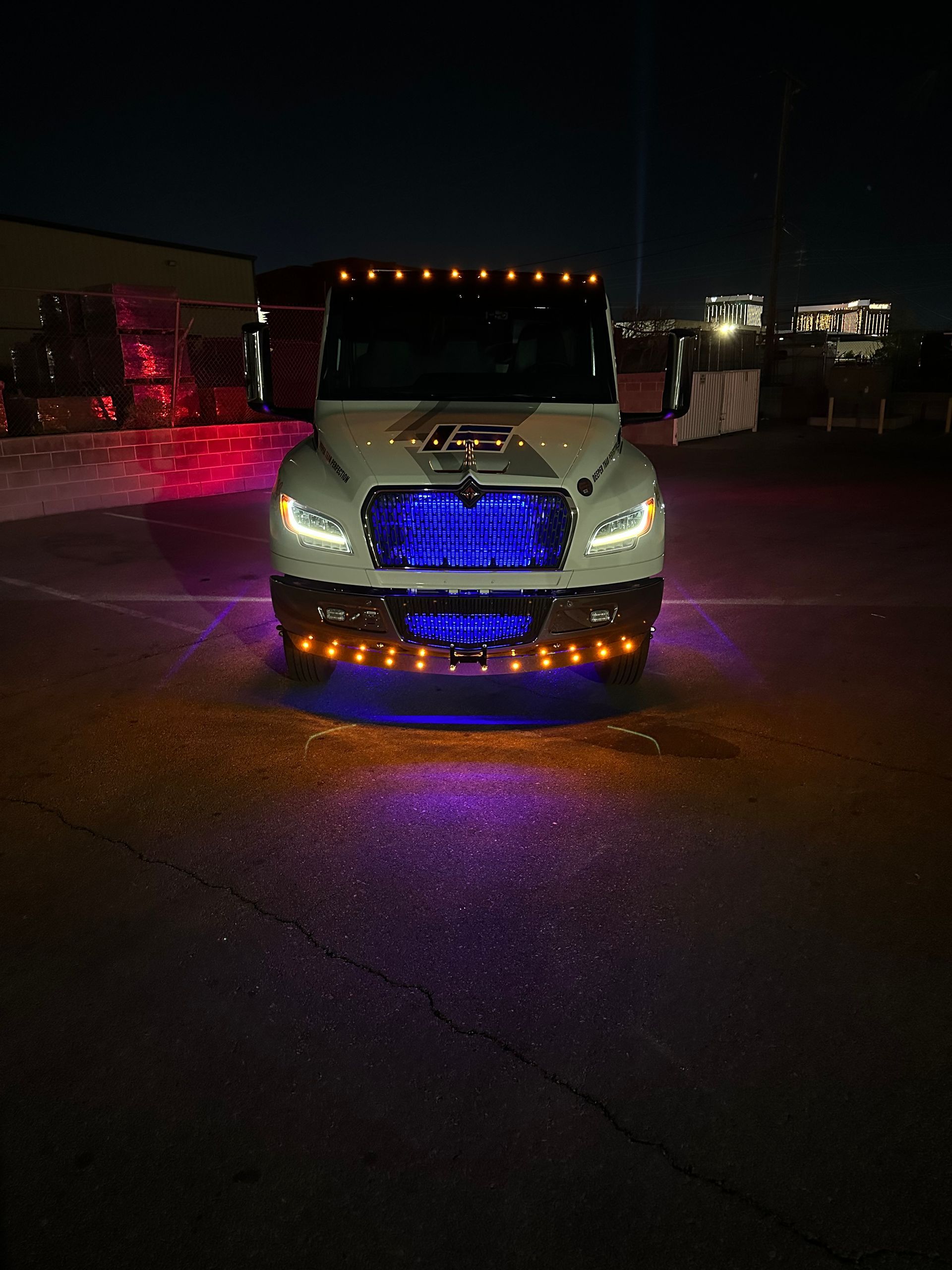 White truck with blue, orange, and purple lights illuminated at night.