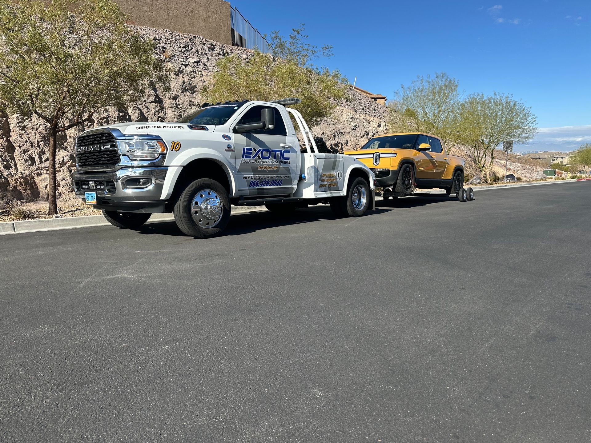Tow truck towing a yellow electric pickup truck on a paved road; sunny day.