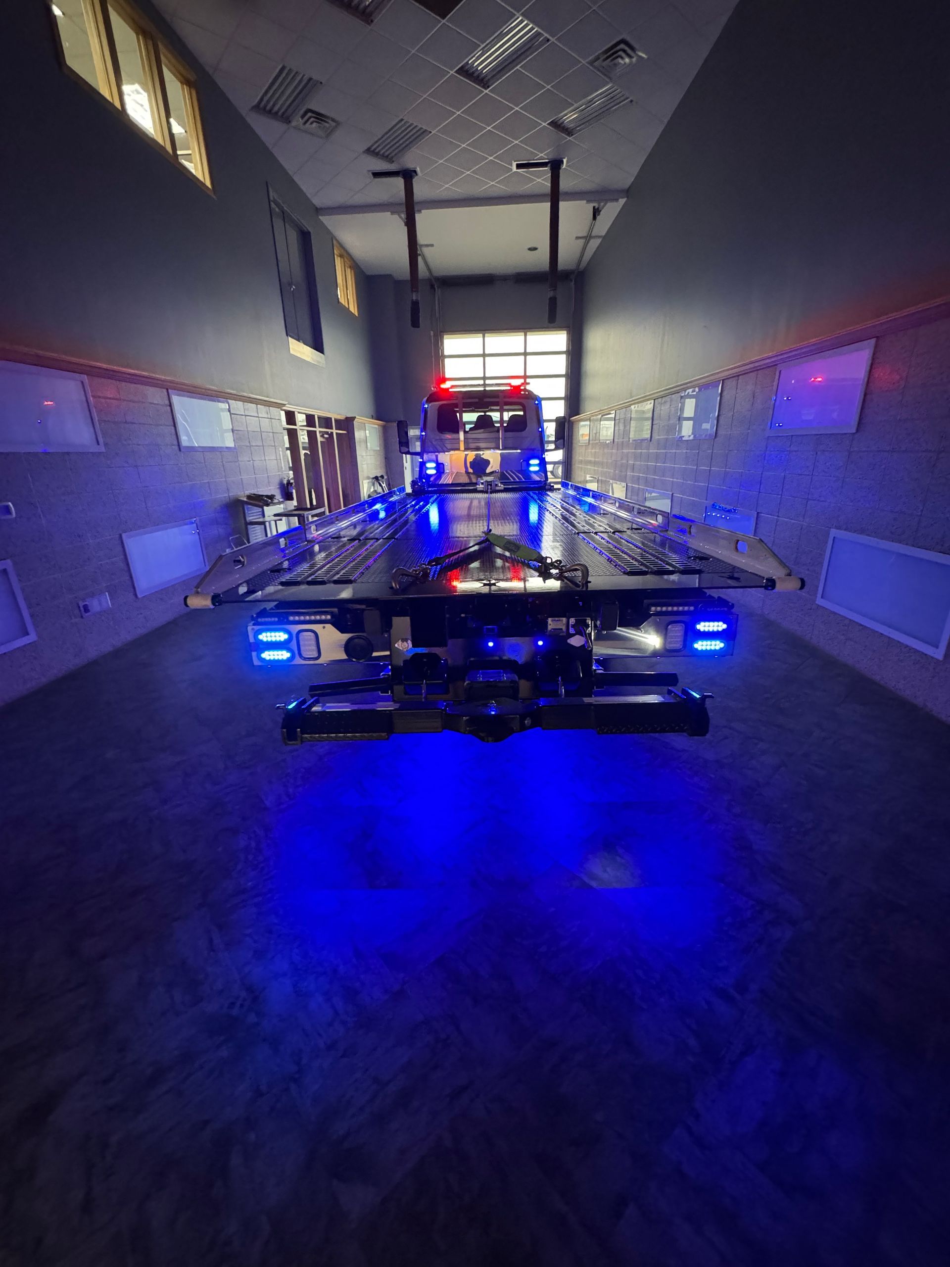 Black flatbed tow truck with blue underglow lights parked indoors.