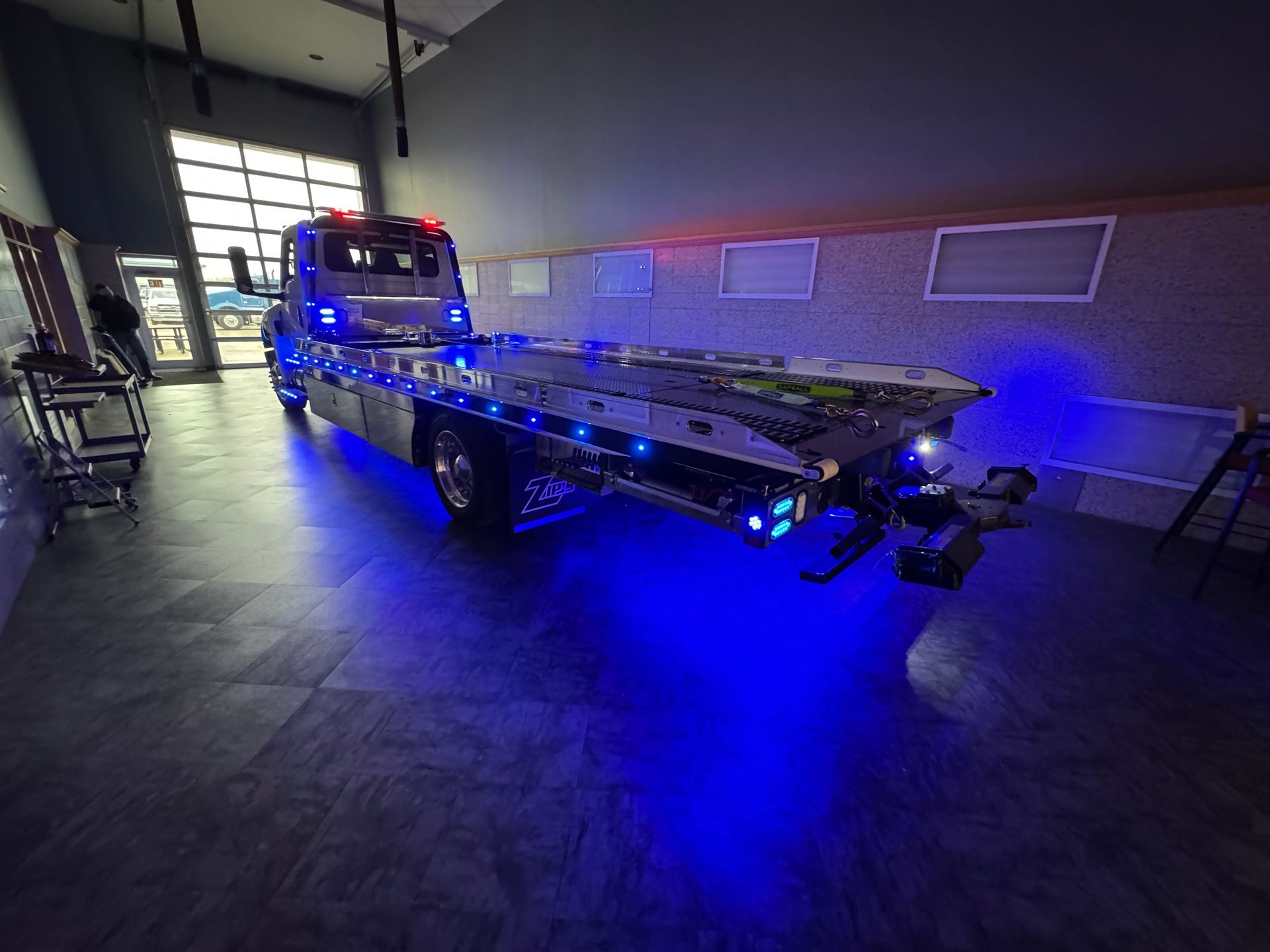 Blue-lit tow truck inside a building, with its flatbed extended.