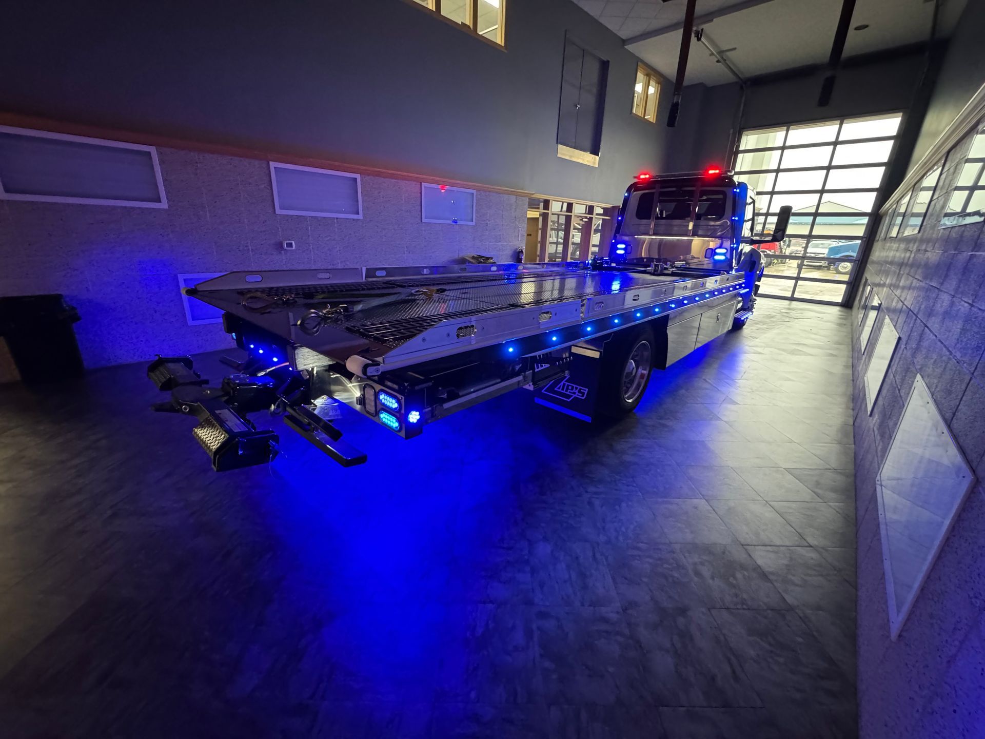 Tow truck with blue underglow lights parked inside a garage.