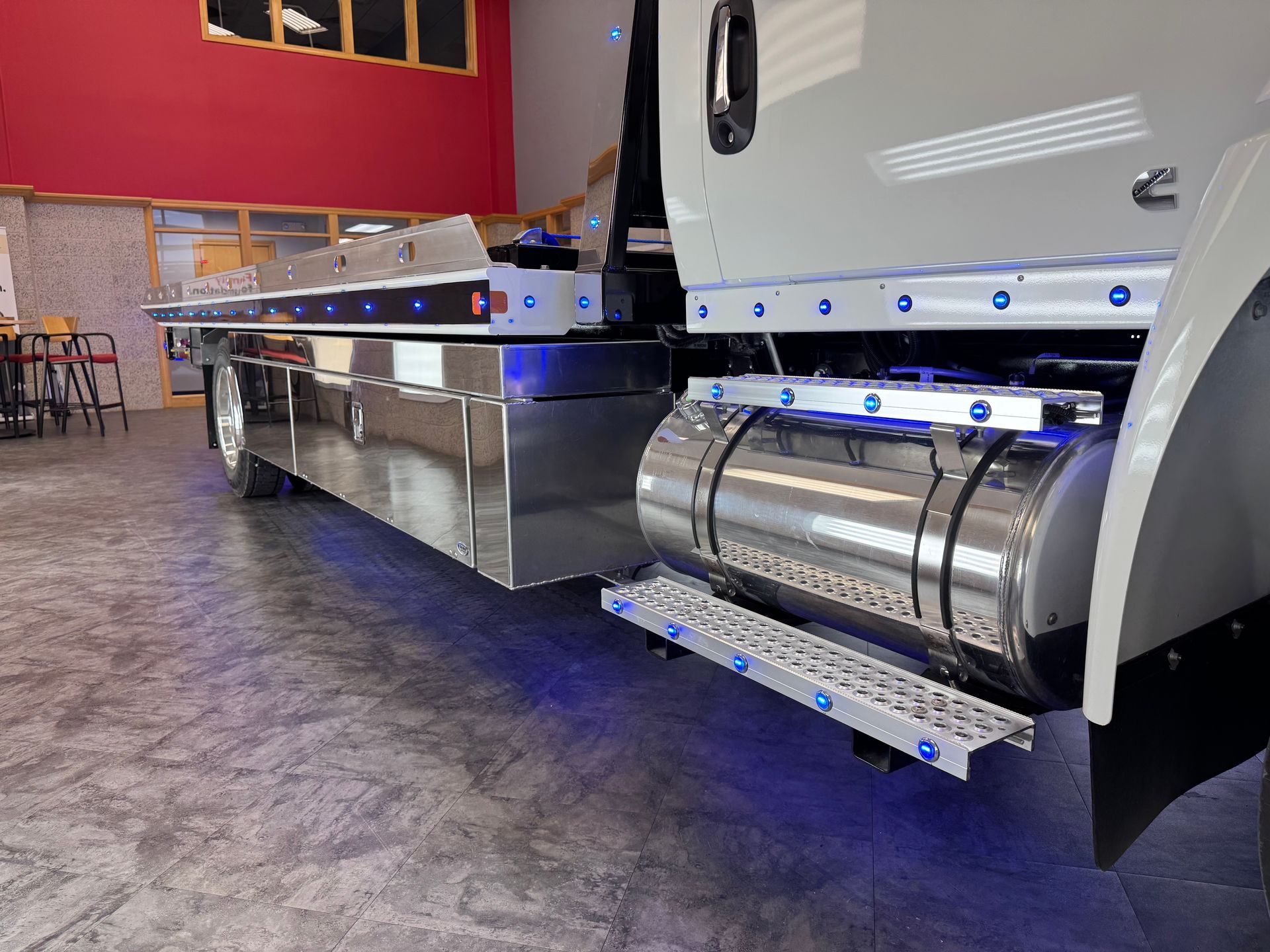 Side view of a white tow truck with chrome details and blue lights in a bright indoor setting.