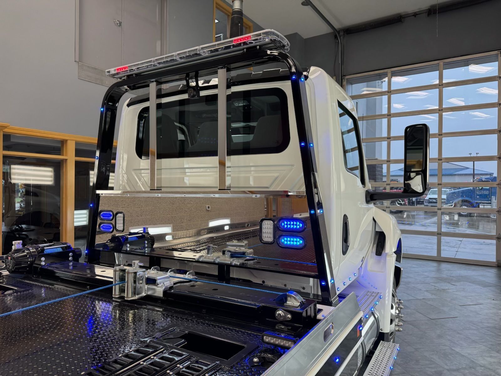 White tow truck with blue lights, parked inside a garage.