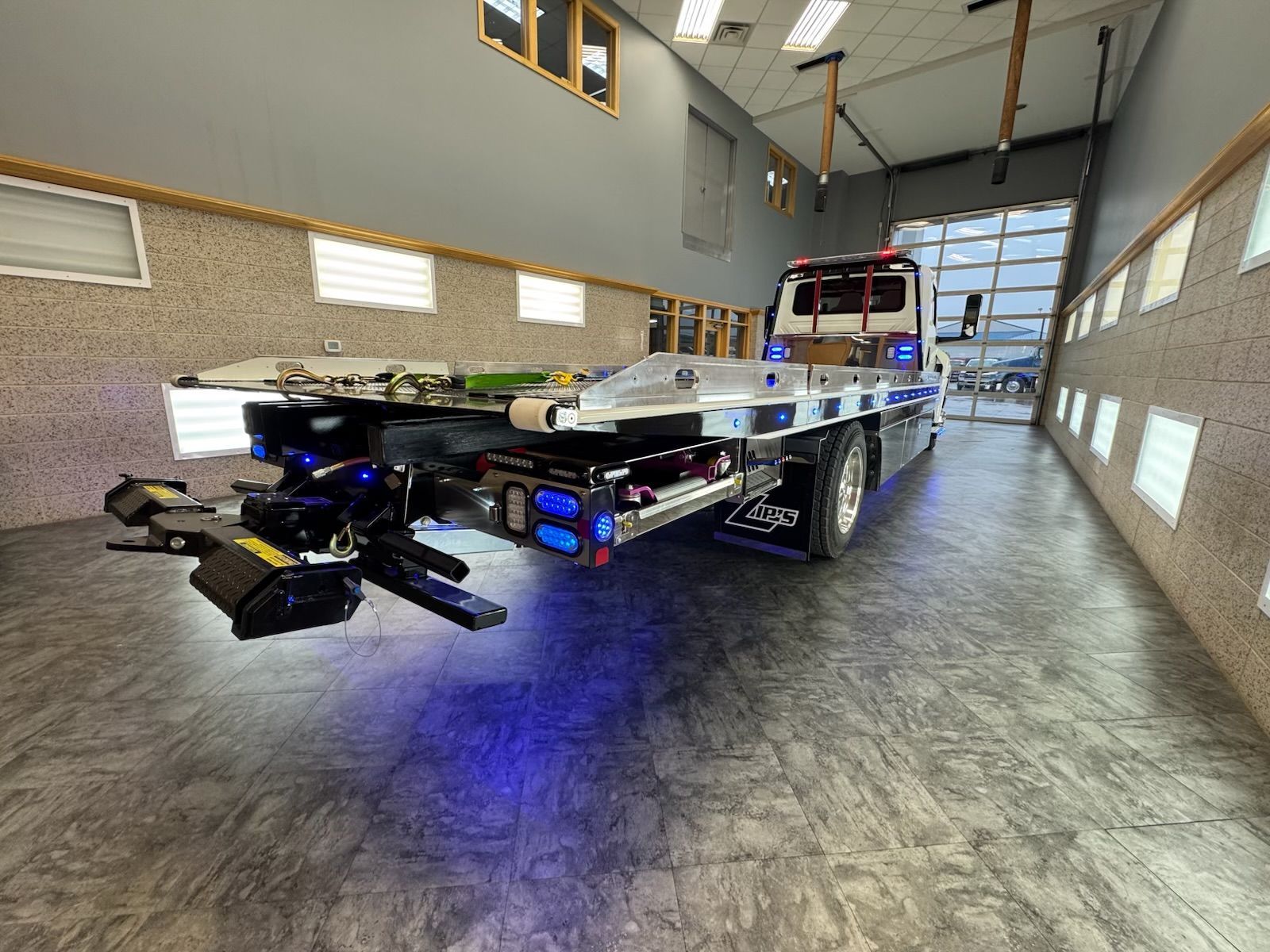 Tow truck with blue underglow parked inside a garage, bed extended.