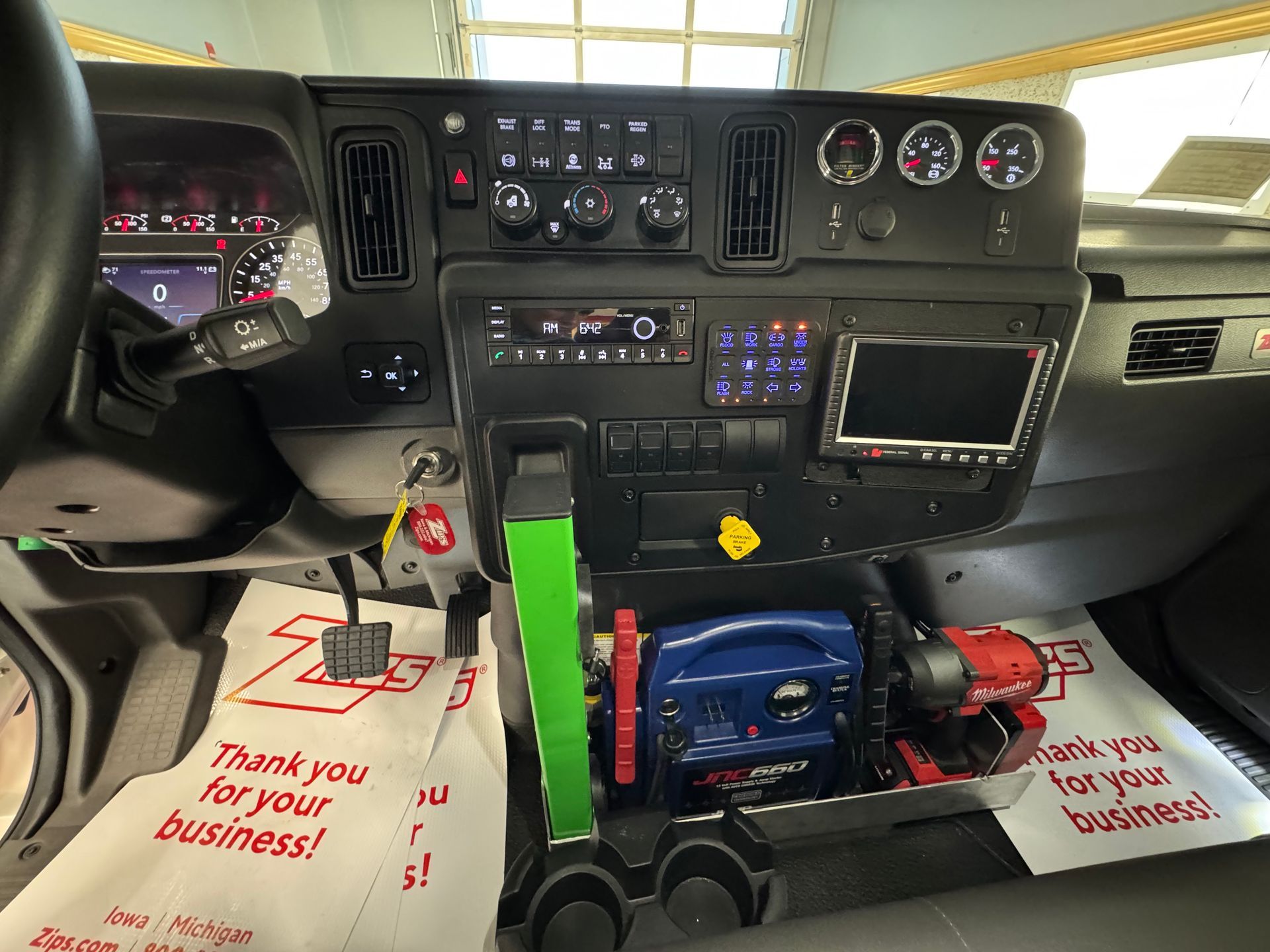 Dashboard of a vehicle with various controls, gauges, and a screen. Some equipment is also stored in the center console area.
