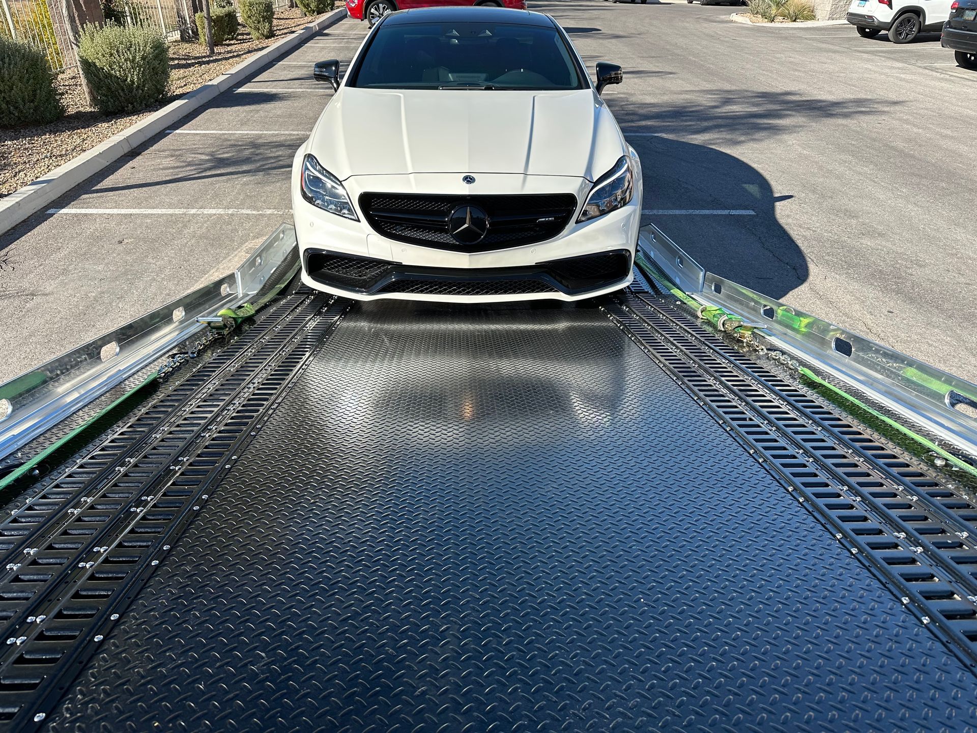White Mercedes car loaded on a black flatbed tow truck outdoors.