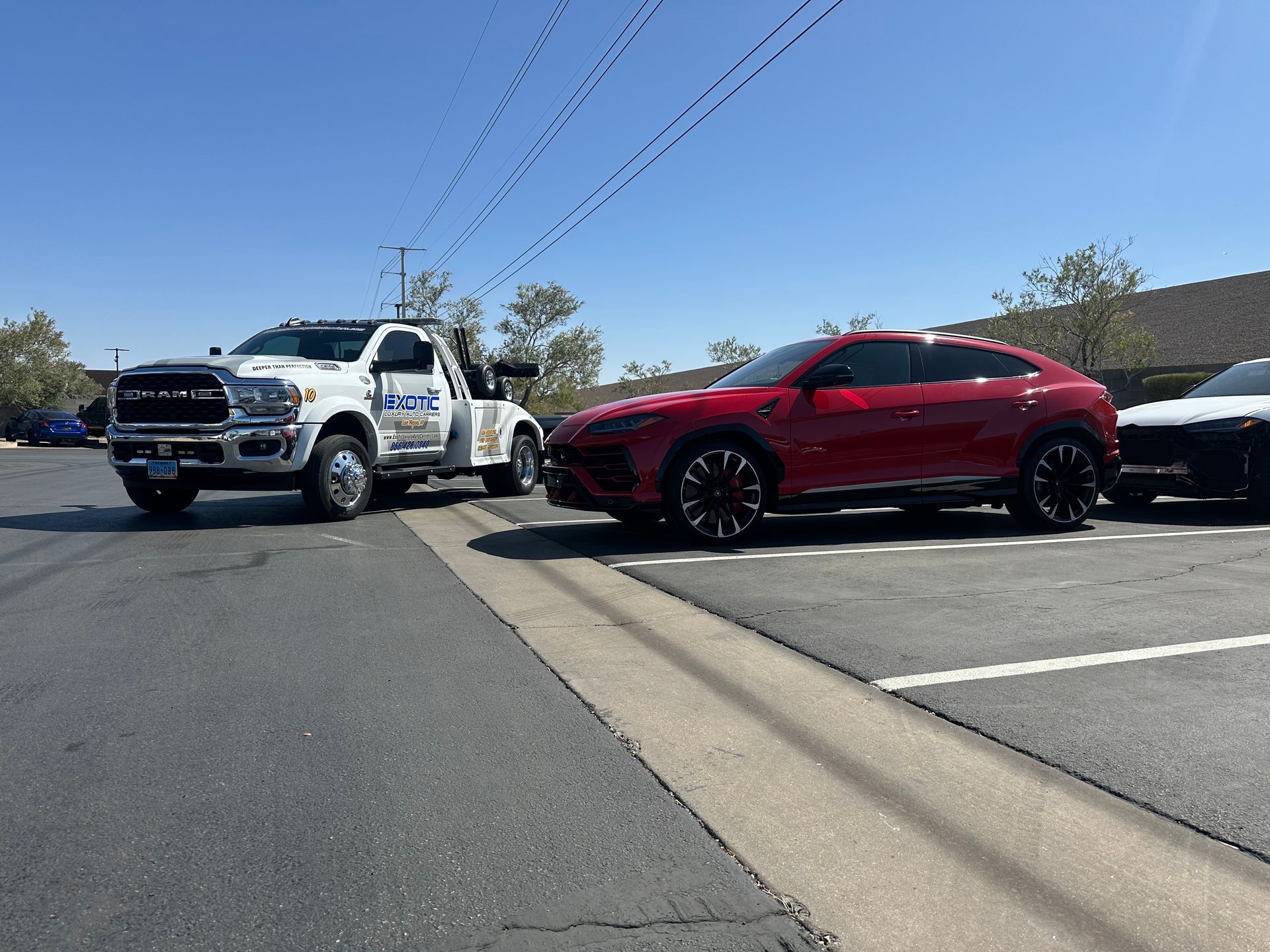 Tow truck towing a red Lamborghini SUV in a parking lot on a sunny day.