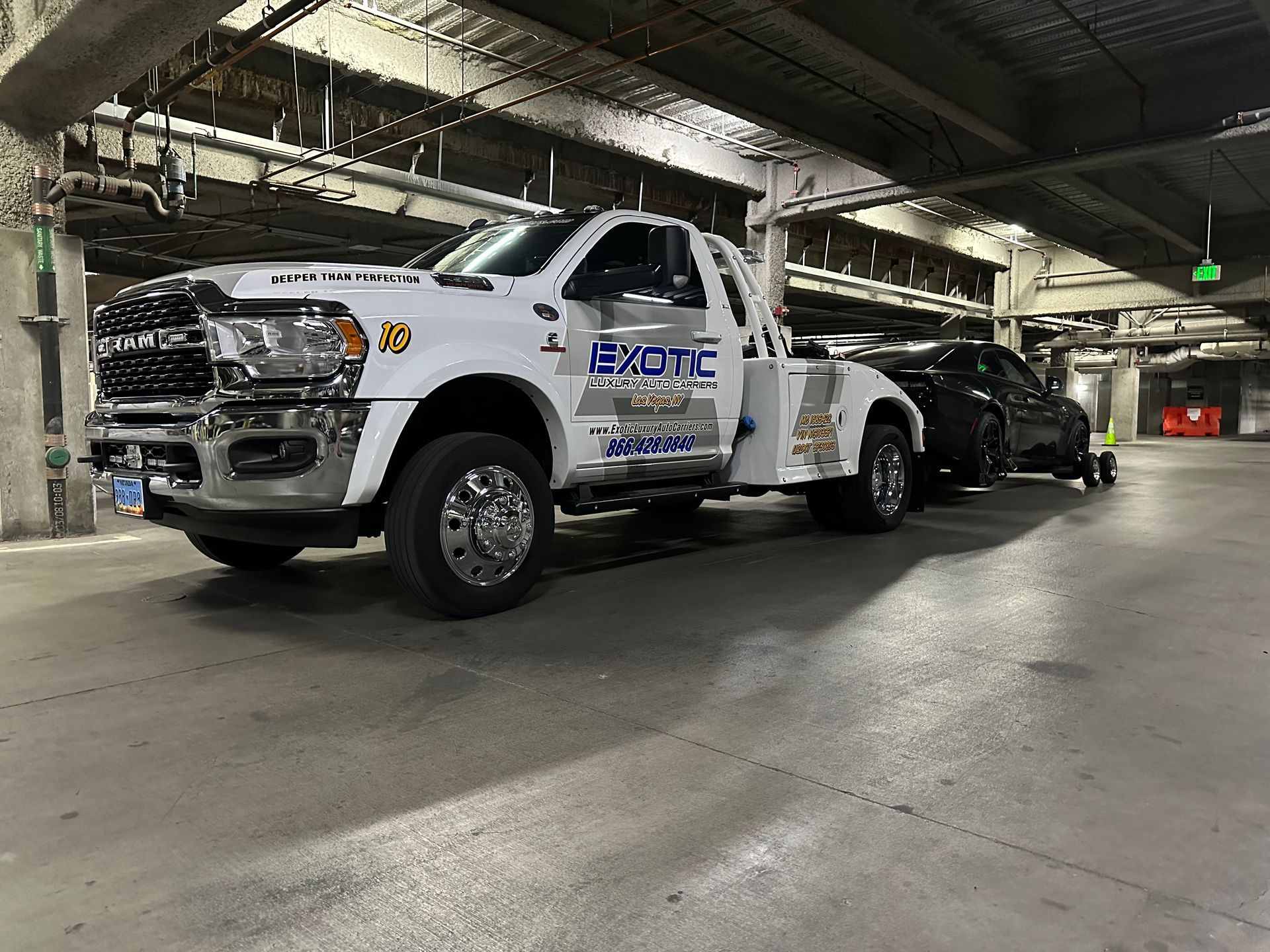 White tow truck towing a black car in a parking garage.