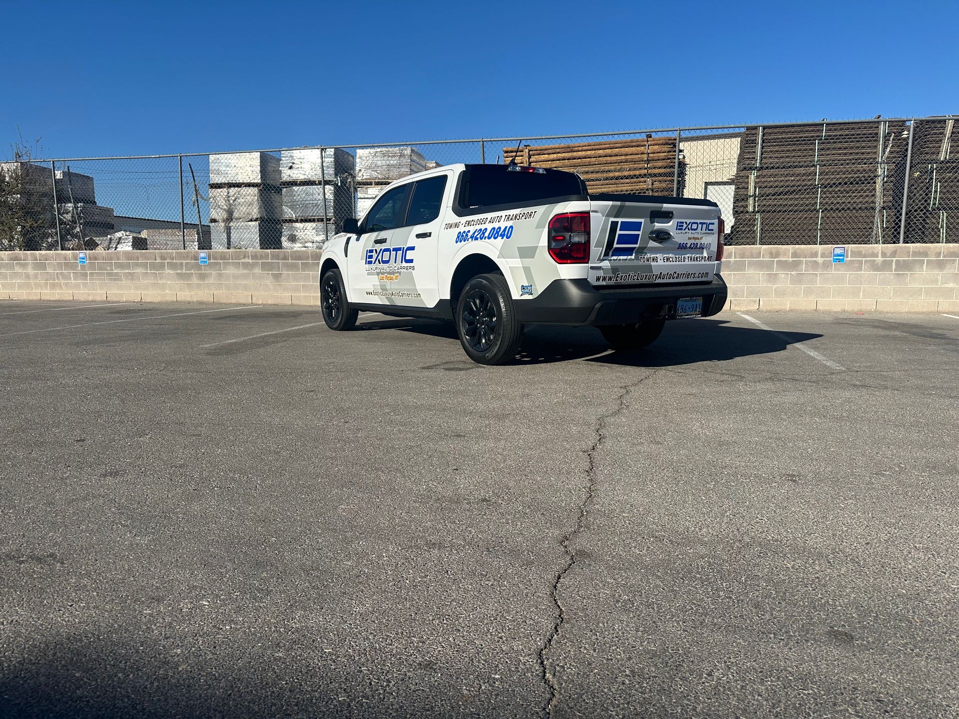 White work truck with black wheels, parked on asphalt, near wooden pallets, sunny day.
