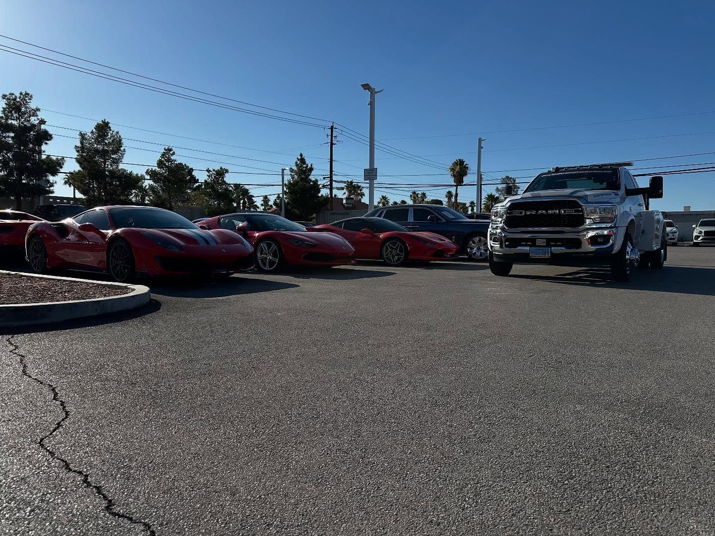Red sports cars parked near a large truck on an asphalt lot under a blue sky.