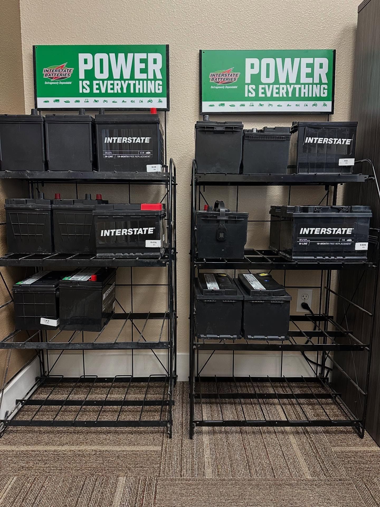 Two black metal shelves displaying car batteries, beneath 