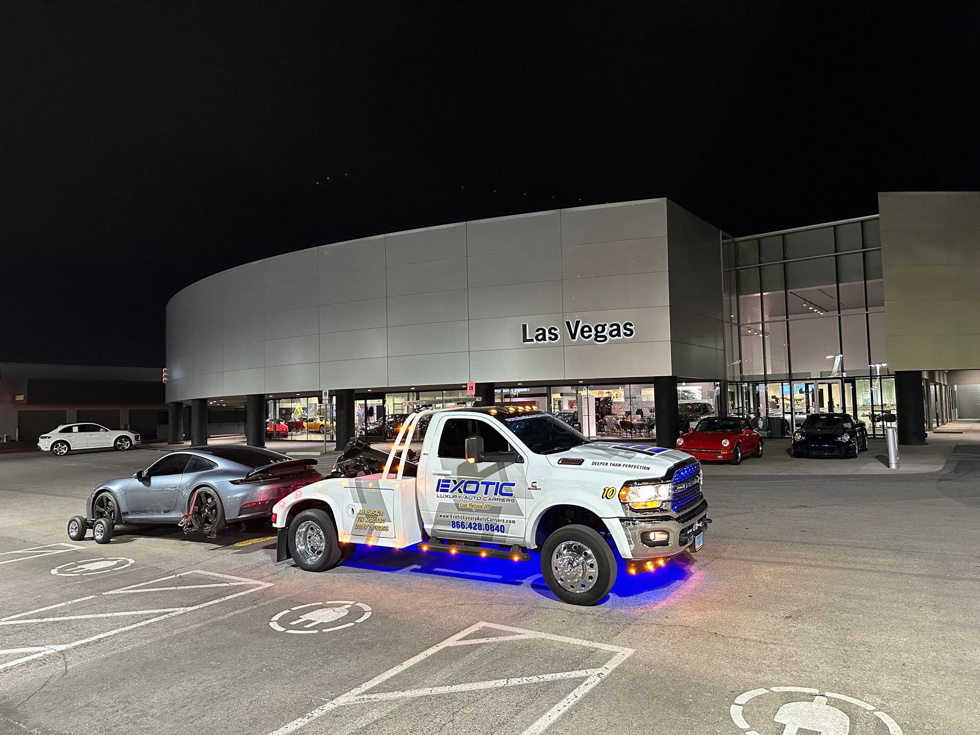 Tow truck towing a gray sports car at night near a building with 