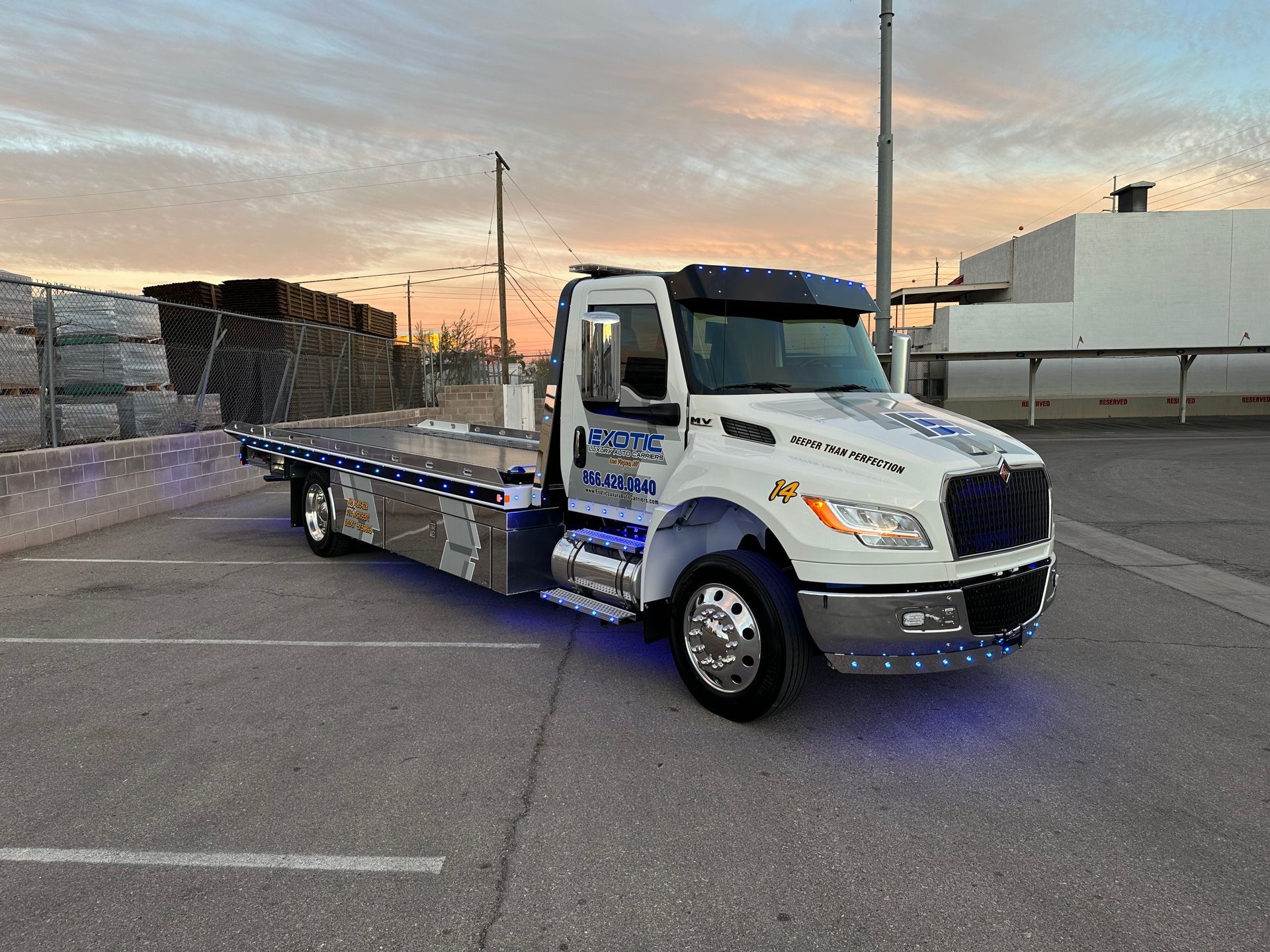 White flatbed tow truck on asphalt at dusk.