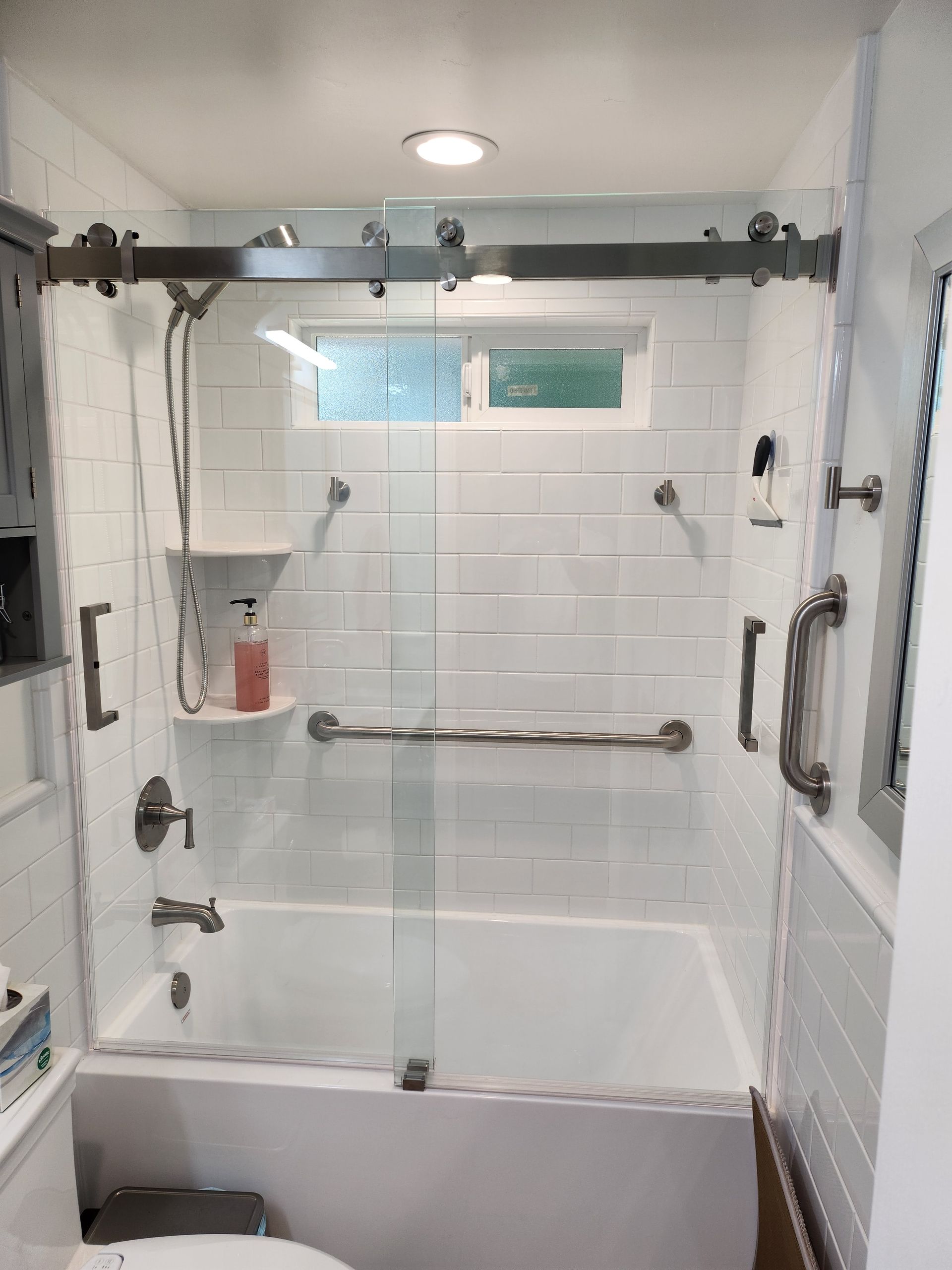 Bathroom with white subway tile, glass shower doors, and grab bars.