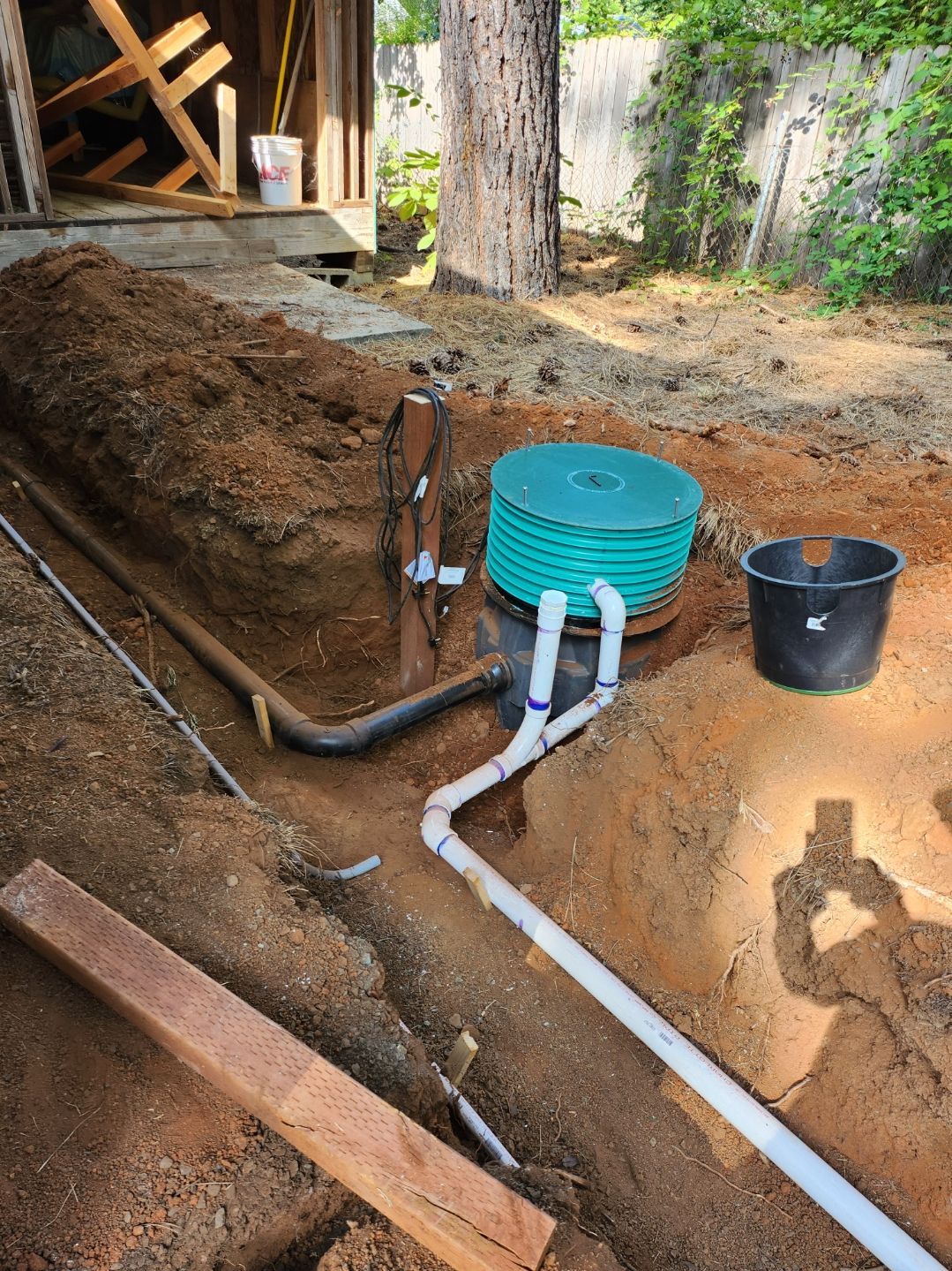 Construction site with buried pipes, coiled tubing, and a bucket. Soil surrounds the plumbing.
