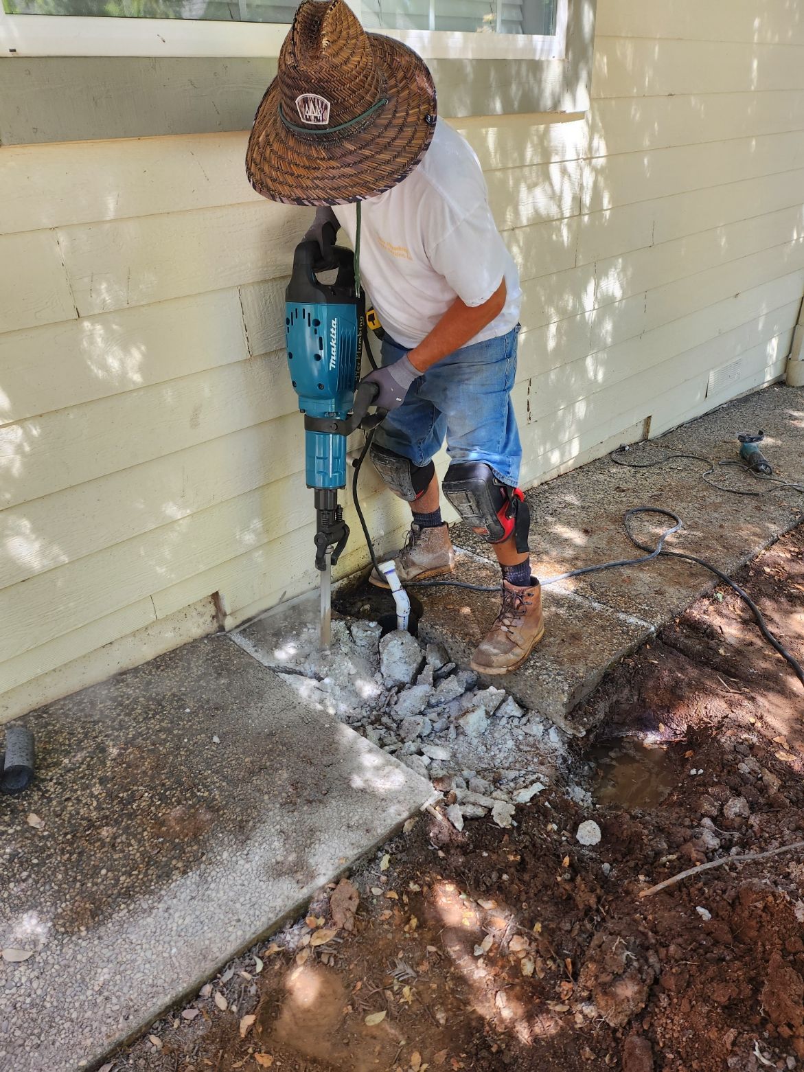Person using a jackhammer to break up concrete next to a building.