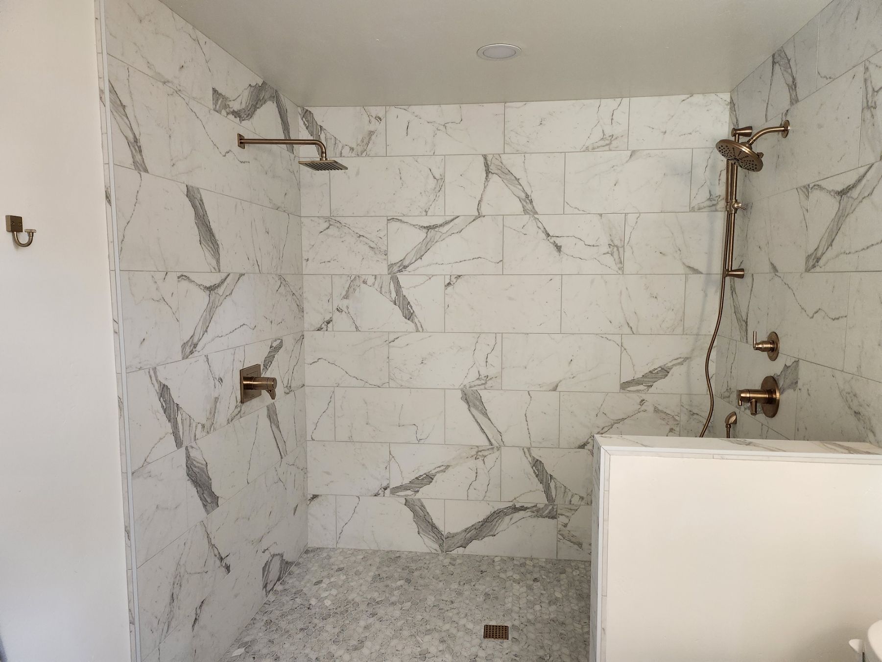 Marble-tiled shower with rose gold fixtures. Gray pebble floor. White walls.