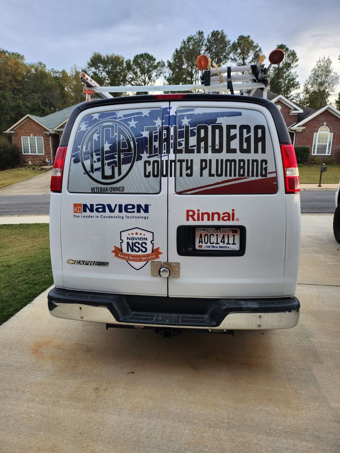 White plumbing van with Talladega County Plumbing logo and equipment on top, parked in a driveway.