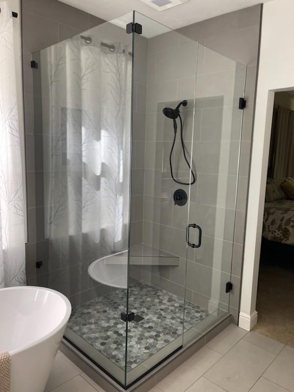 Glass shower enclosure with gray tile, black fixtures, and a curved bench.