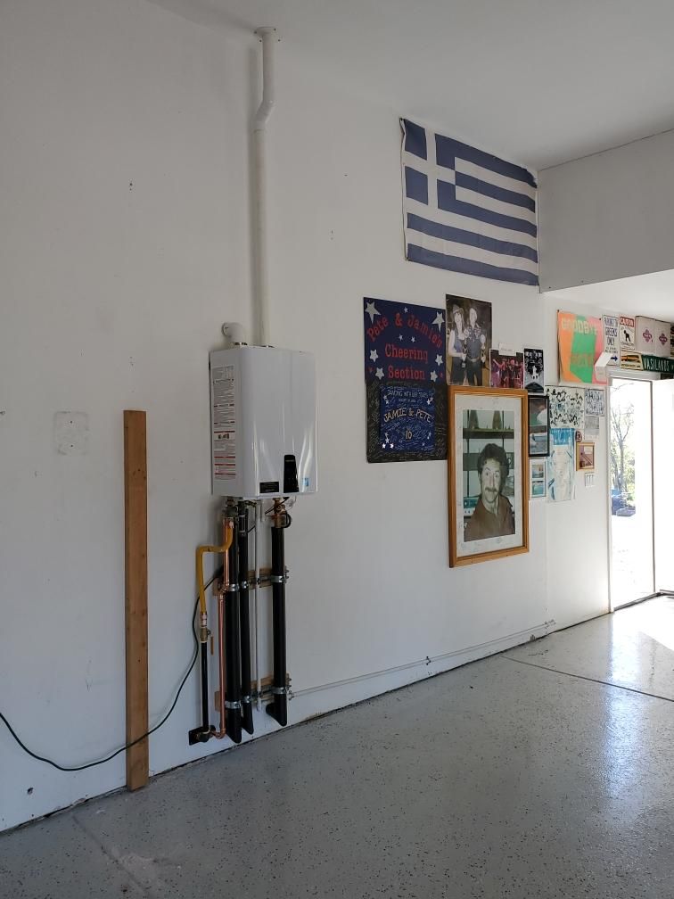 White wall with tankless water heater, Greek flag, framed art, and open garage door.