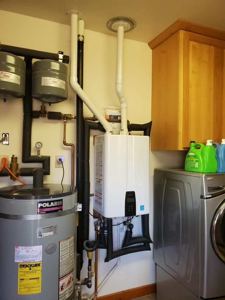 Water heater and related piping in a laundry room, with a washing machine and cabinets visible.