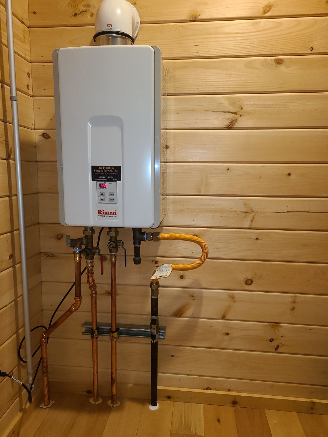 Tankless water heater installed on a wood-paneled wall. Copper pipes and gas line connected.