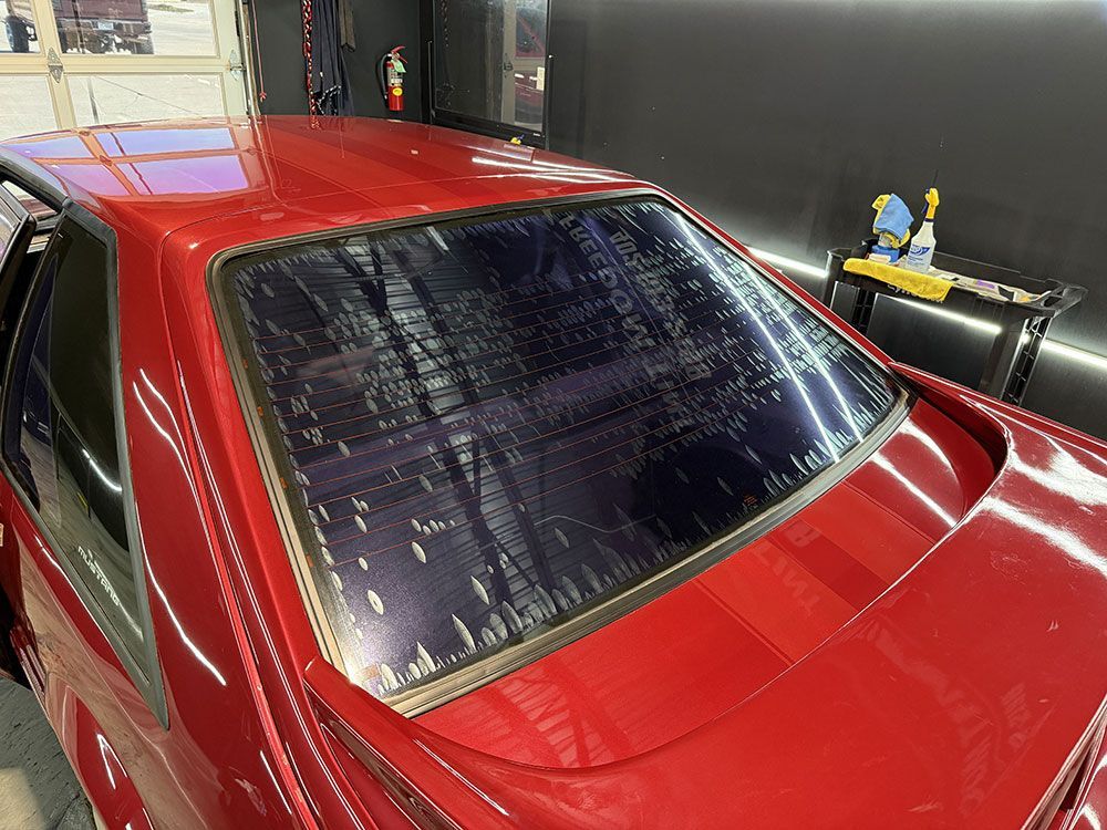 A red car with a black window is sitting in a garage.