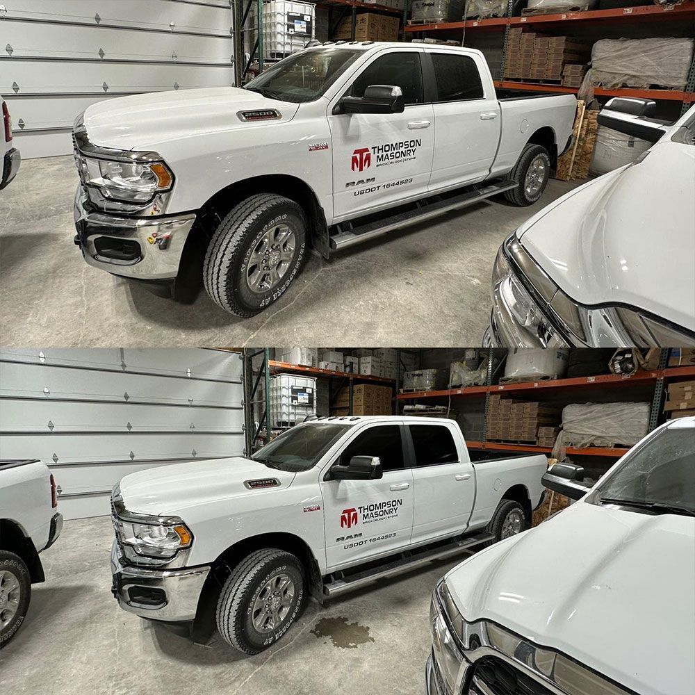 A white truck is parked in a garage next to another truck.