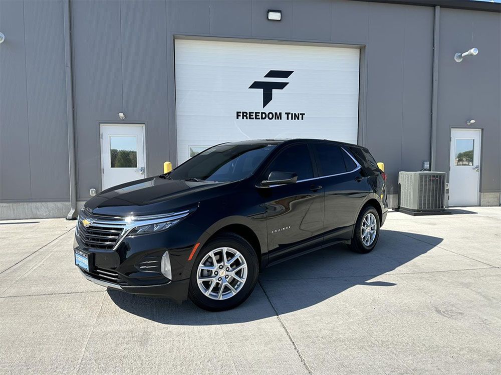 A black chevrolet equinox is parked in front of a garage door.