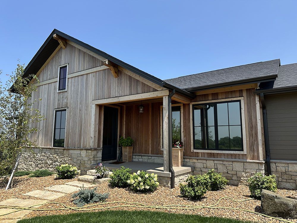 The front of a house with a wooden siding and a stone wall.