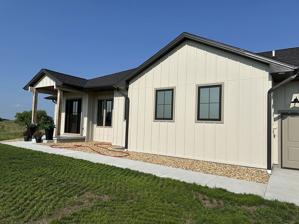 A white house with black windows is sitting on top of a lush green field.
