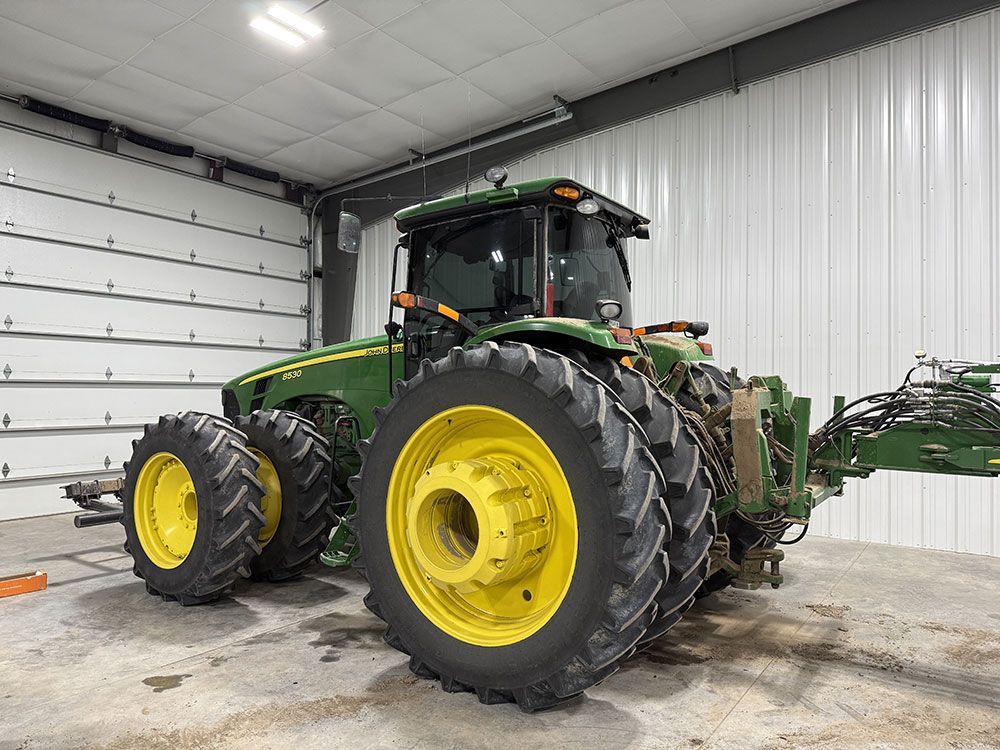 A green and yellow john deere tractor is parked in a garage.