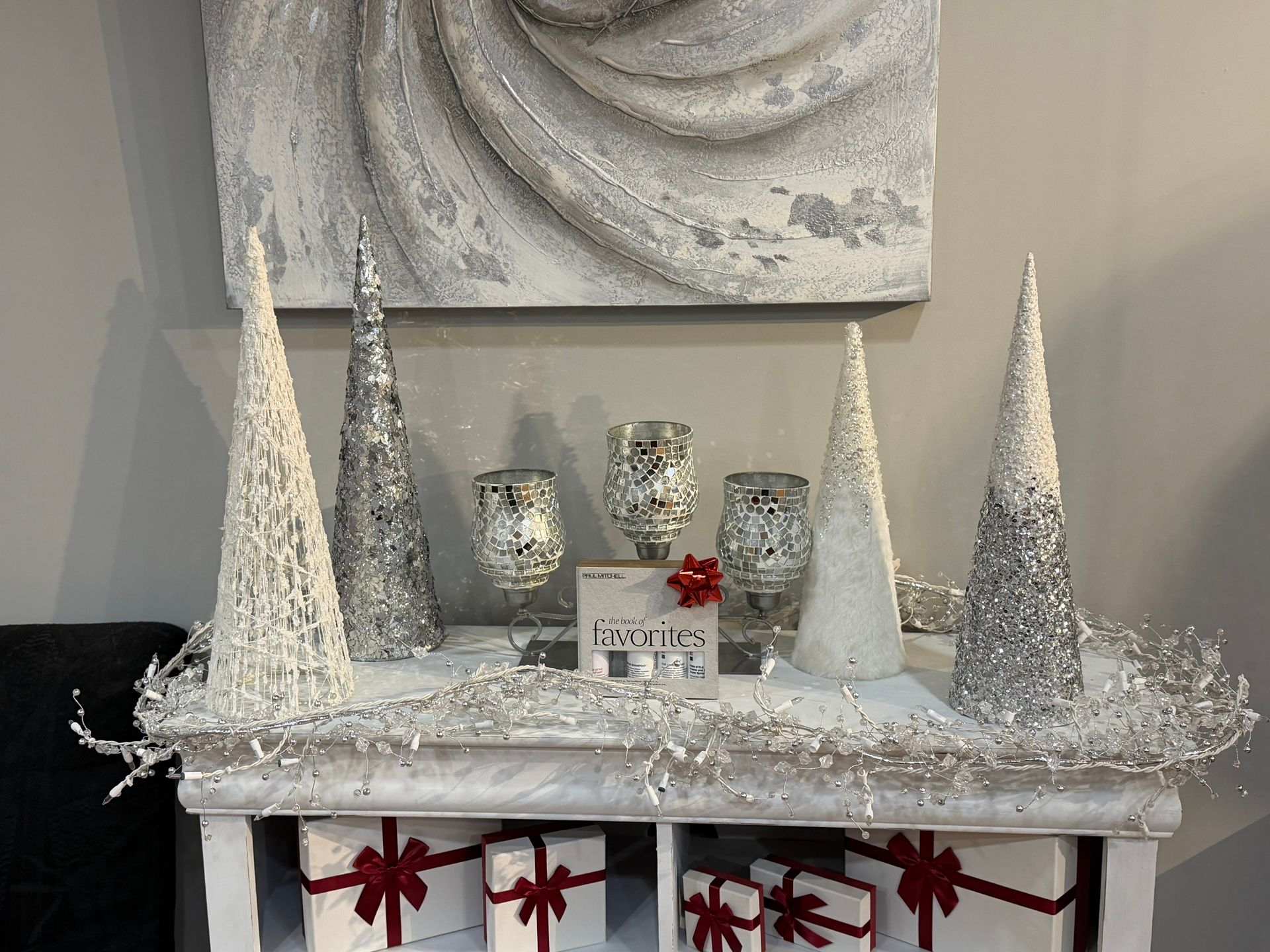 White and silver Christmas display on a white shelf, decorated with snowy trees and garland, and gift boxes.