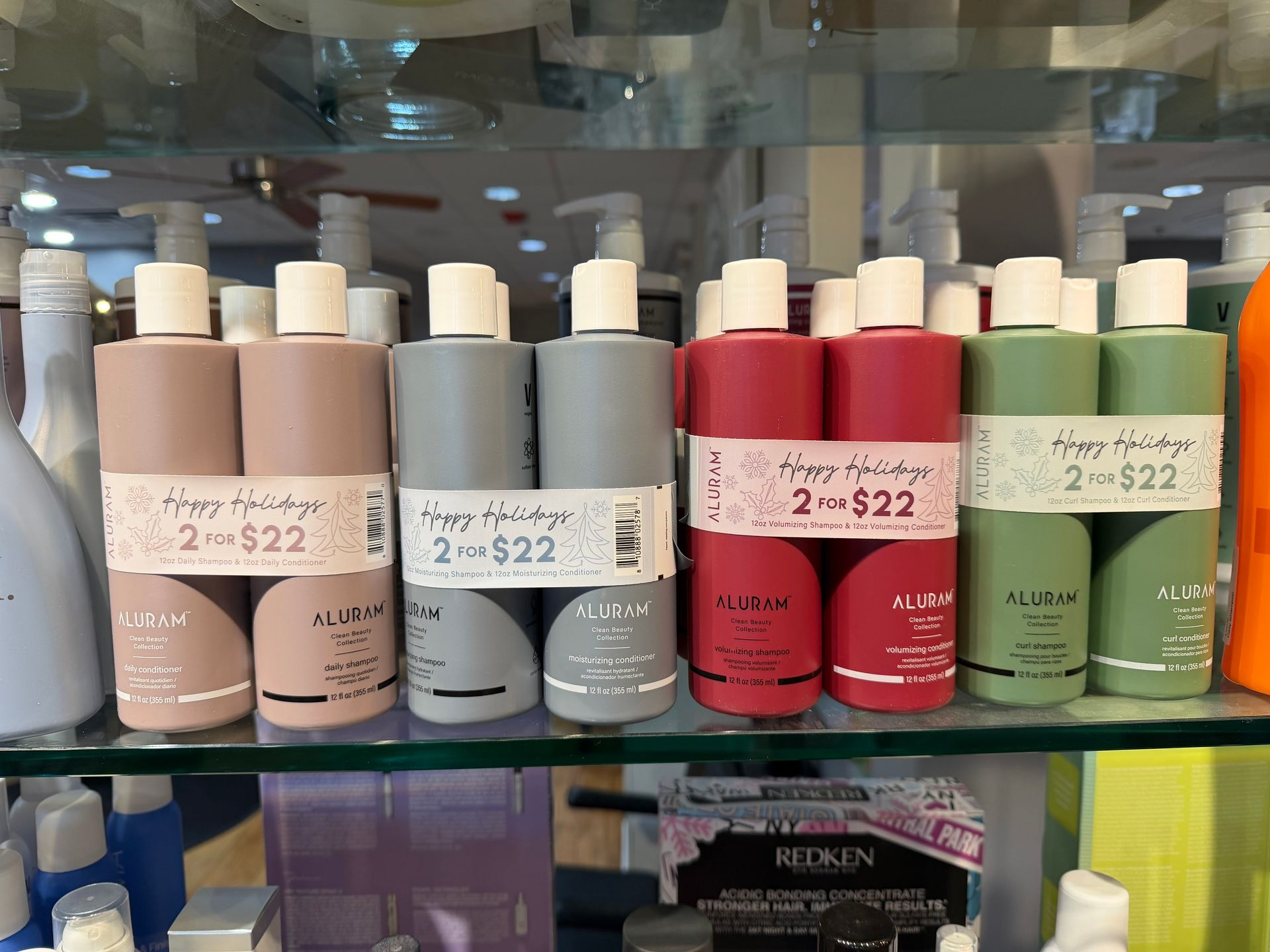 Bottles of hair products, in various colors, are for sale on a shelf with a “Happy Holidays 2 for $22” price tag.